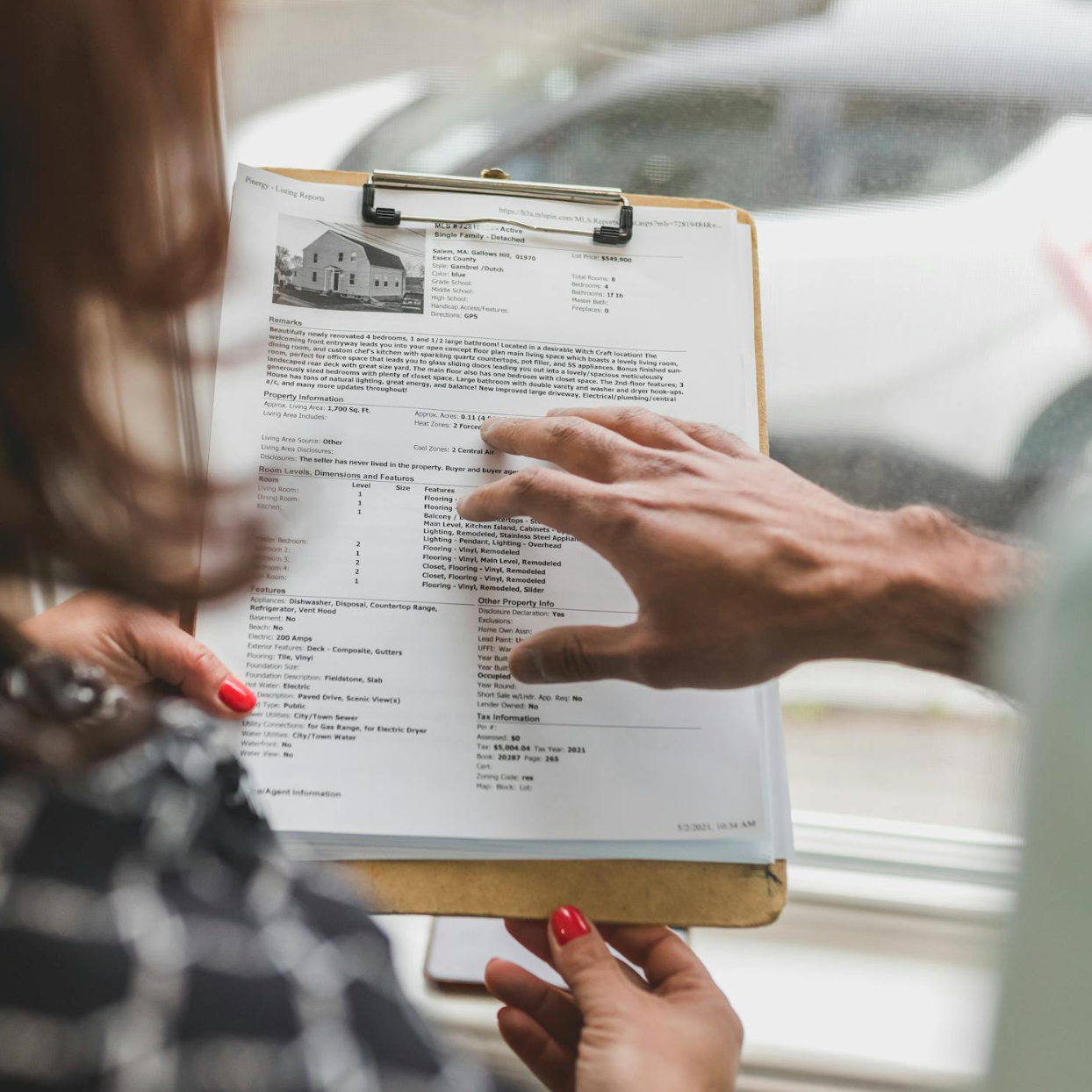 Person pointing at a property listing report on a clipboard as another person holds it.