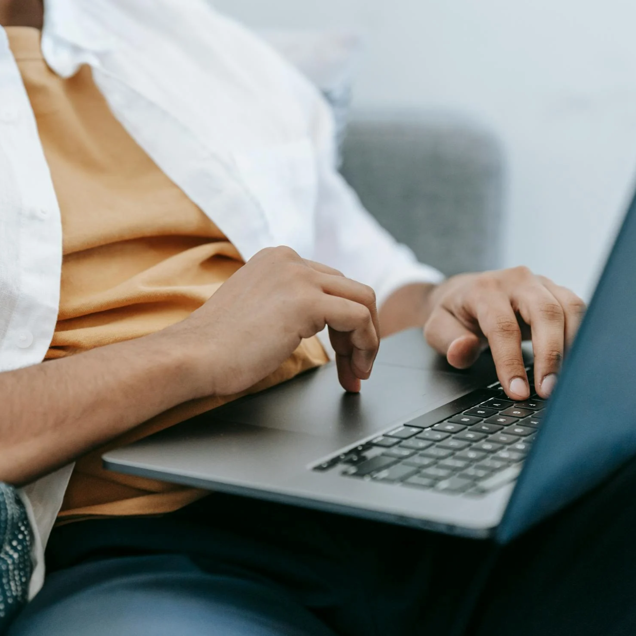 Close-up of a person typing on a laptop keyboard while seated.