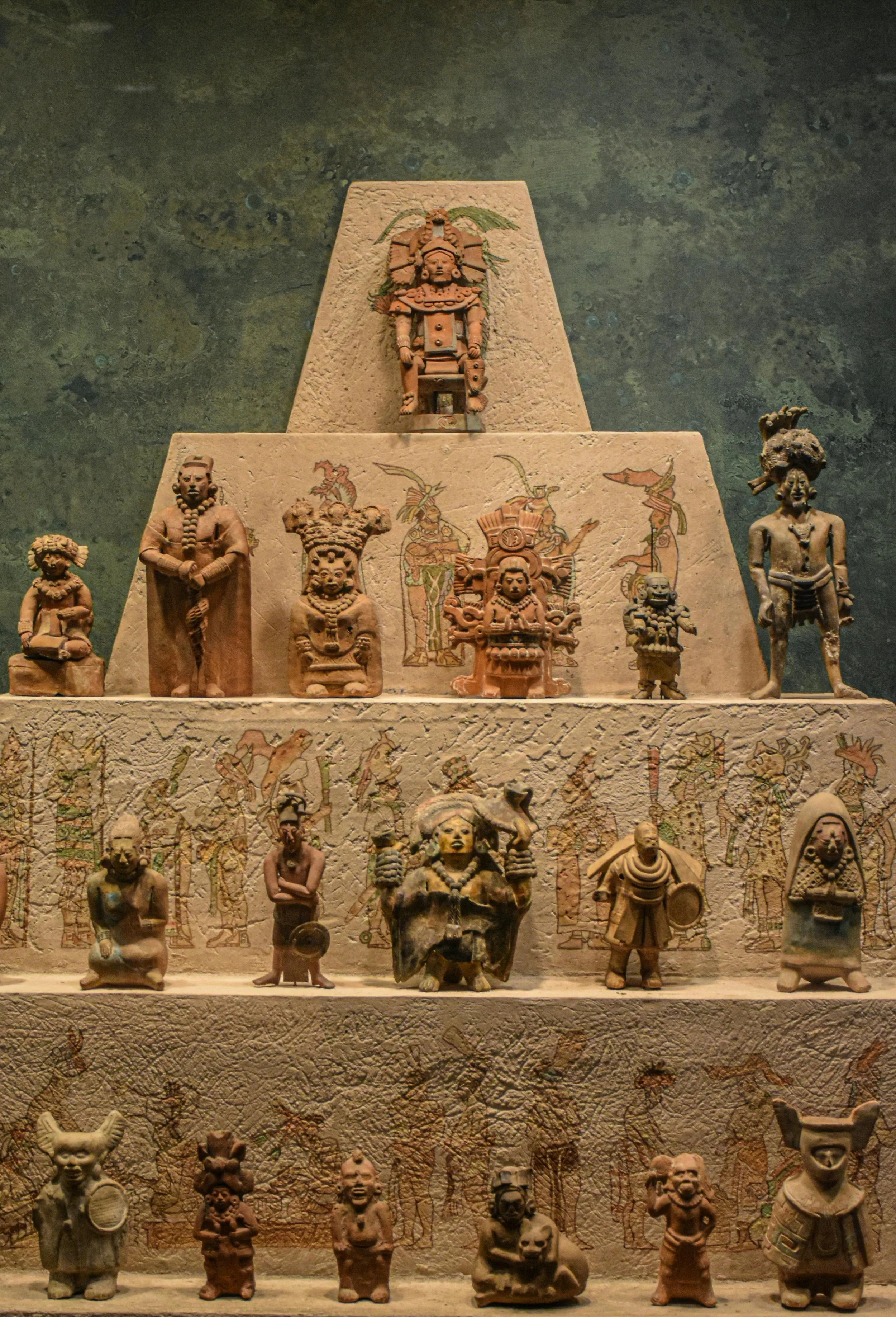 Various ancient clay figurines and sculptures displayed on tiered shelves, depicting human and mythological figures with intricate designs and colorful painted details.