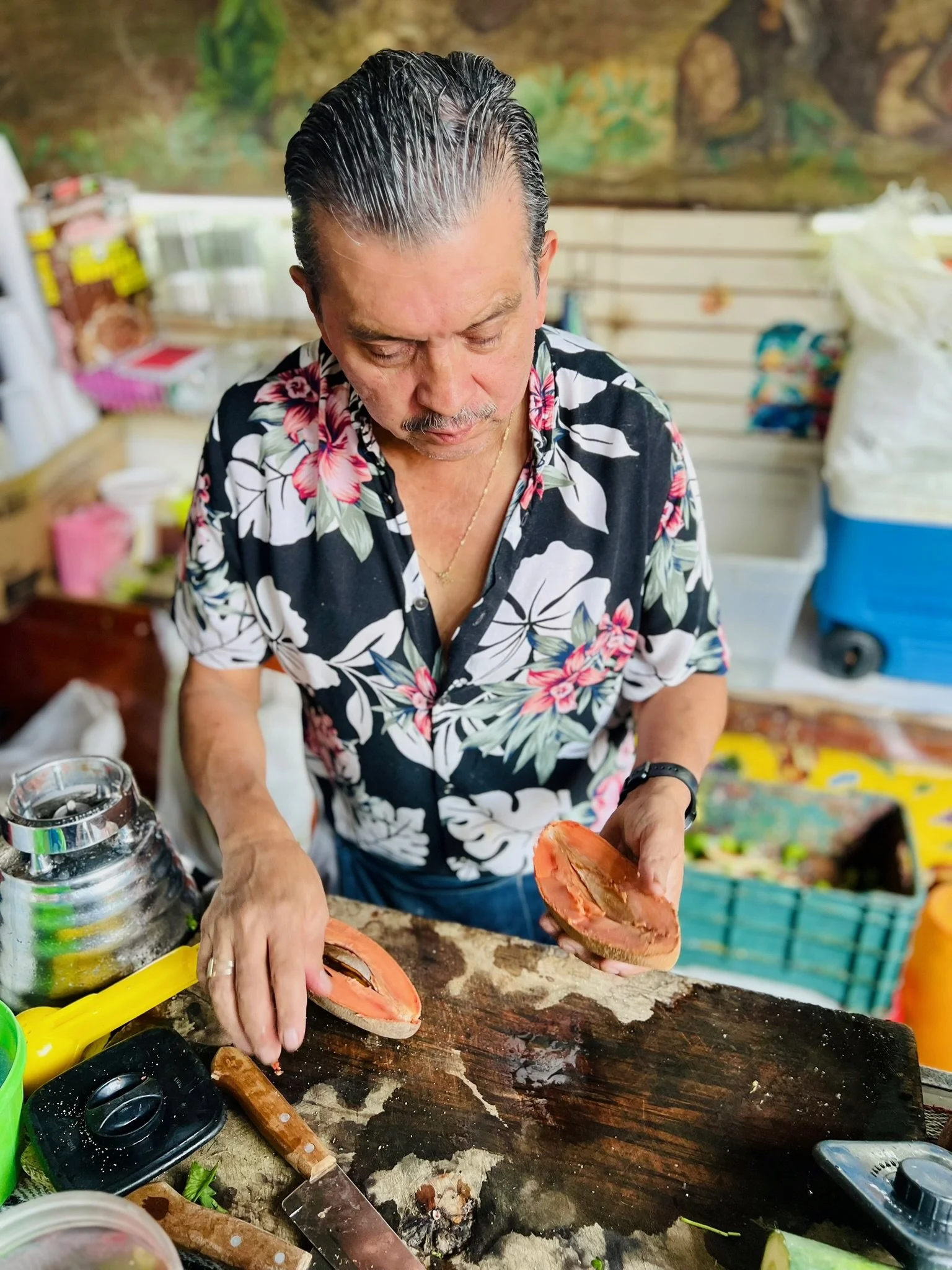 Man in a floral shirt preparing seafood at a market stall.