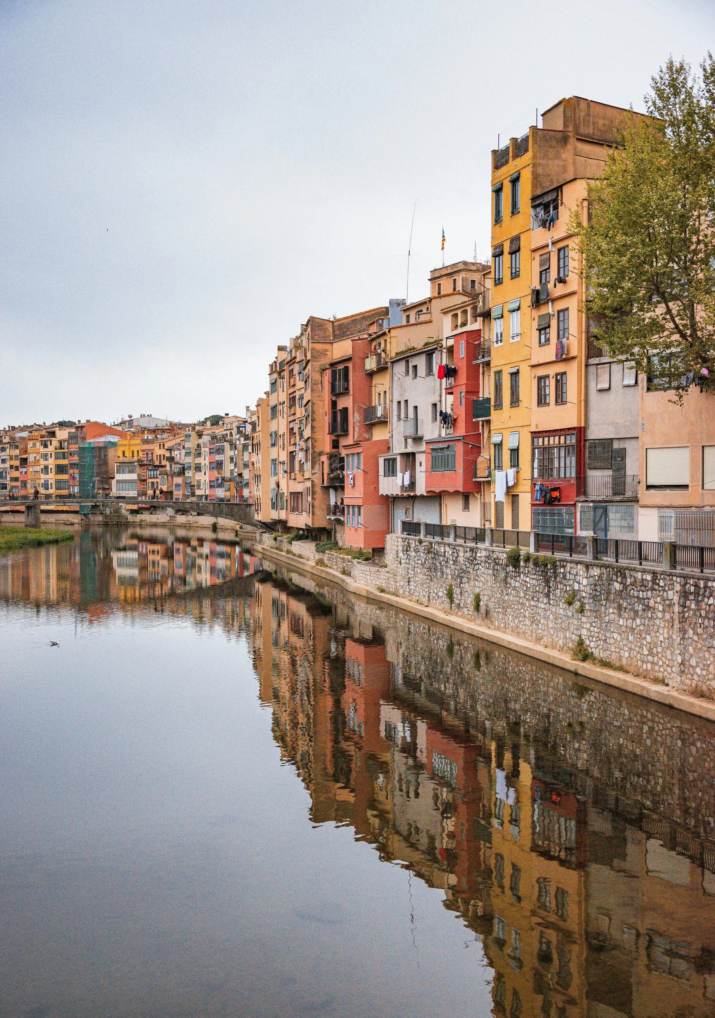 Colorful apartment buildings along a river, with their reflections visible in the water and an overcast sky above.