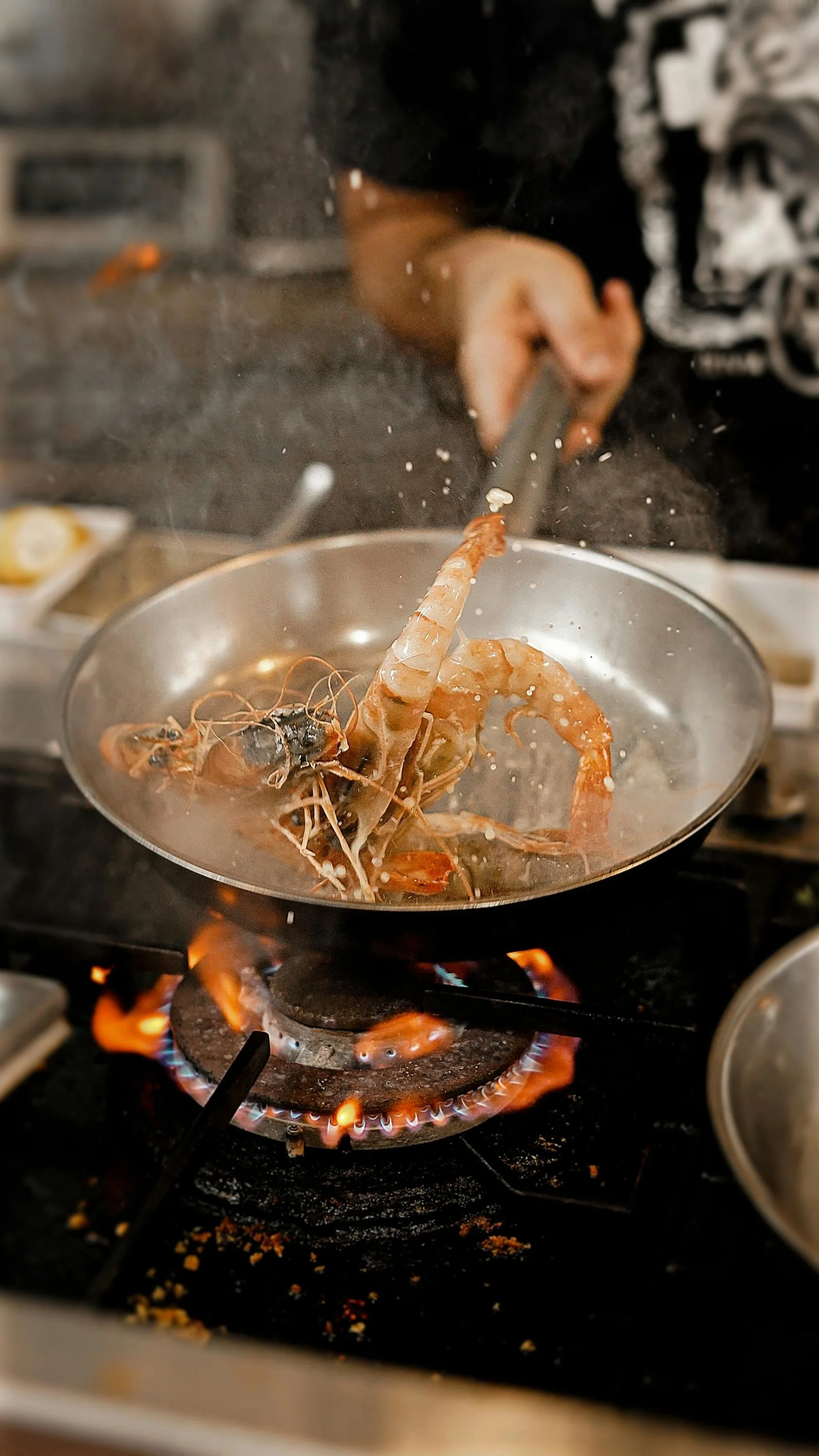 Person cooking shrimp in a frying pan over an open flame stove.