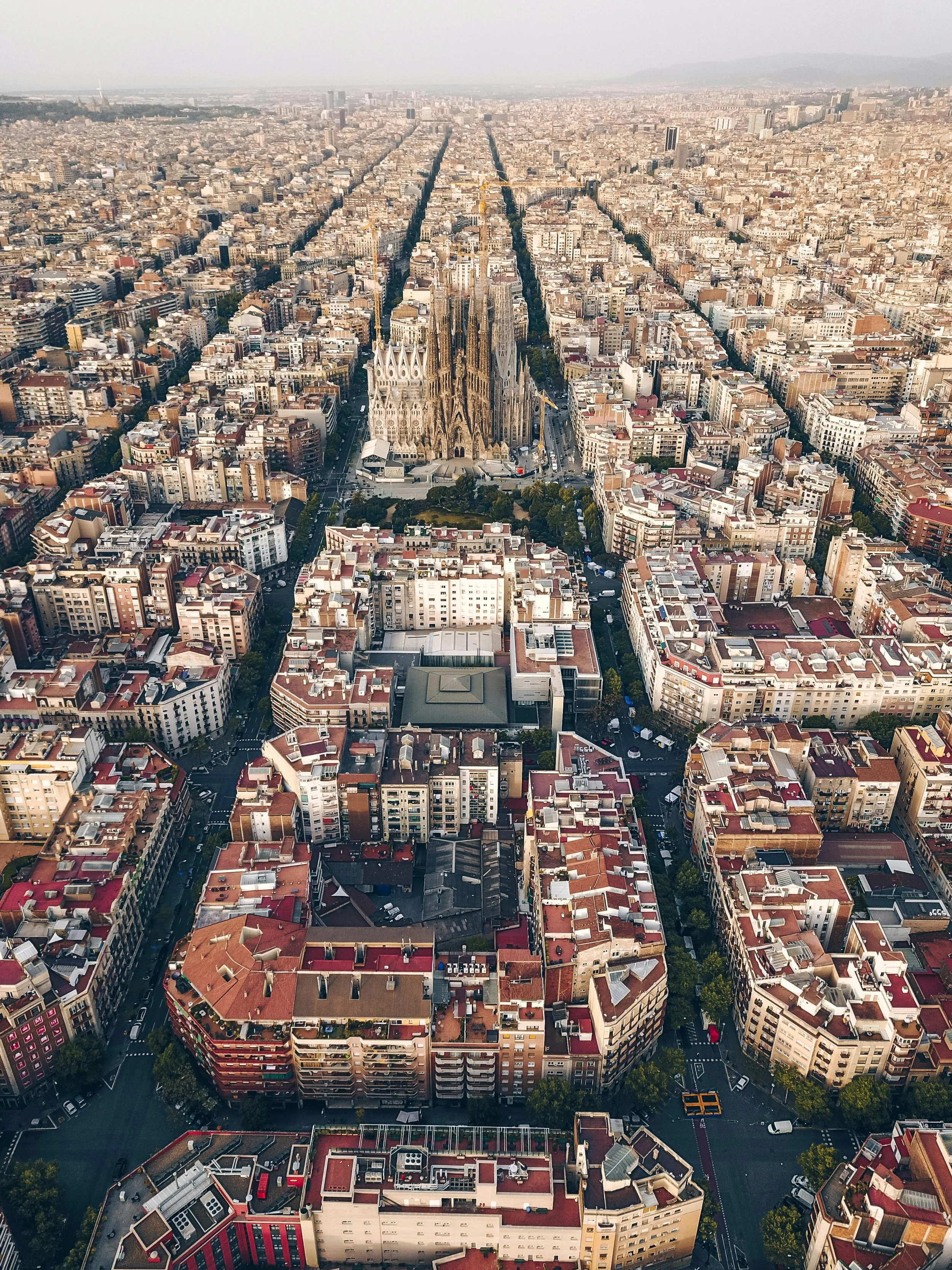 Aerial view of Barcelona, Spain, featuring the Sagrada Família basilica with a cityscape of densely packed buildings and streets.