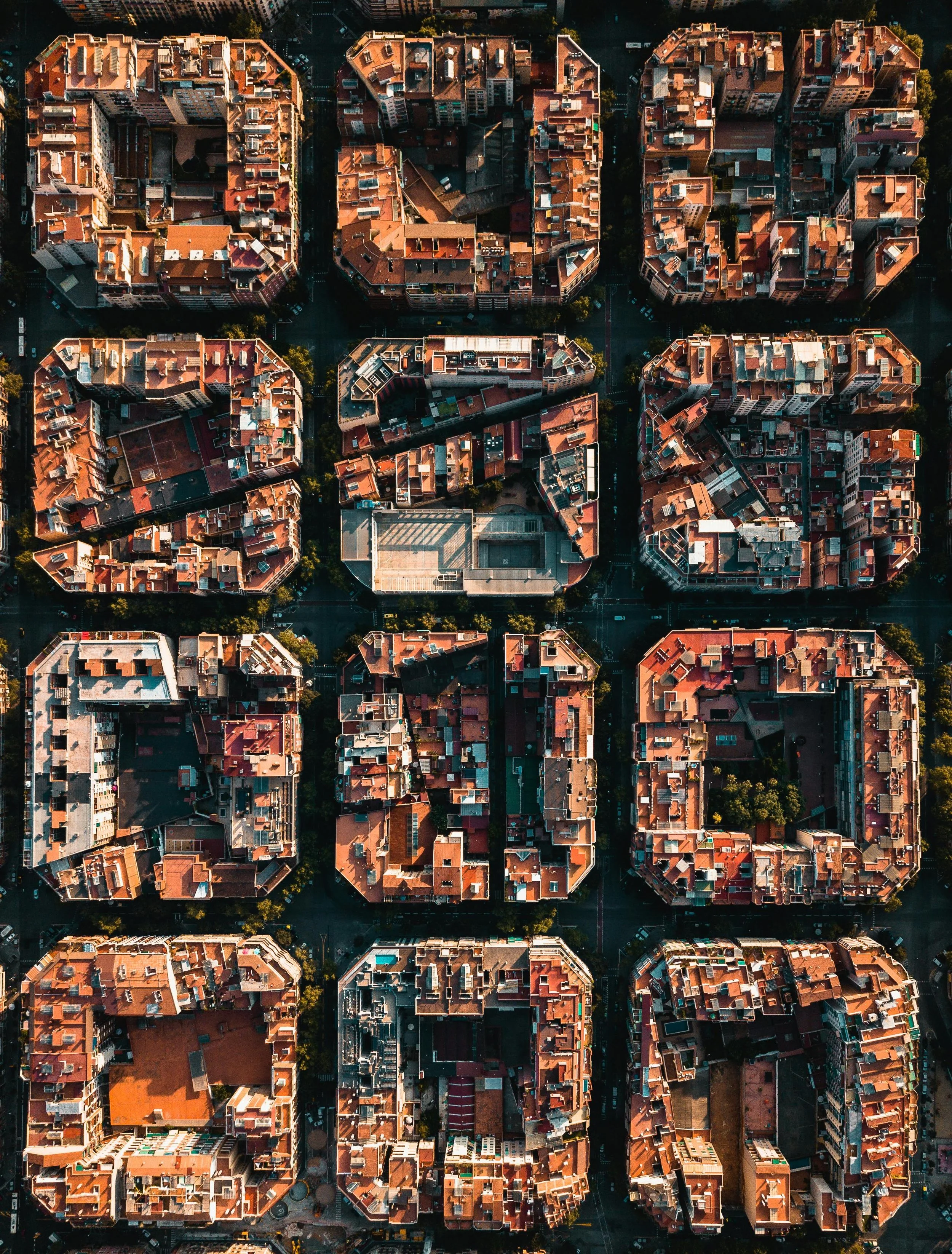 Aerial view of a grid of apartment buildings with red-tiled roofs in a city, showing streets and some green spaces between structures.
