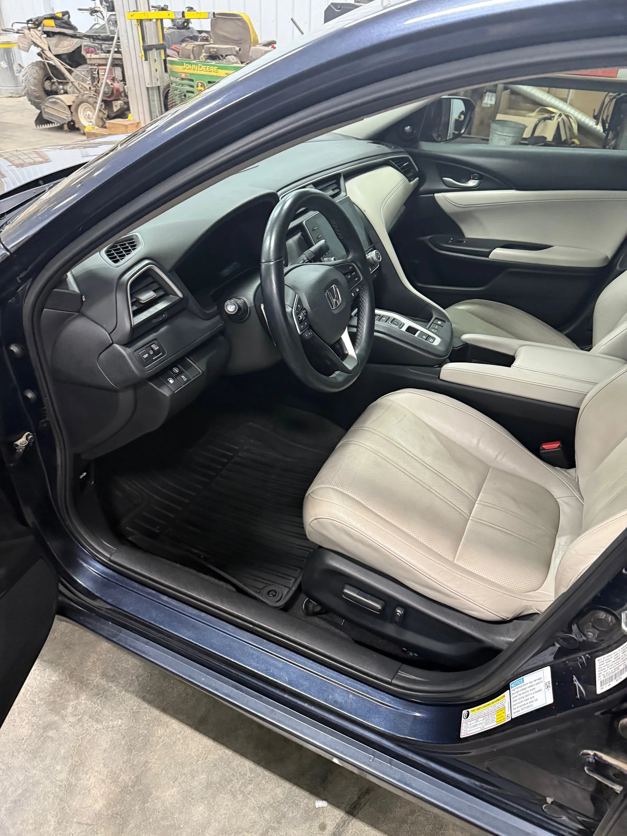Interior of a black Honda car showing the driver's seat, steering wheel, dashboard, and front passenger seat with beige upholstery.