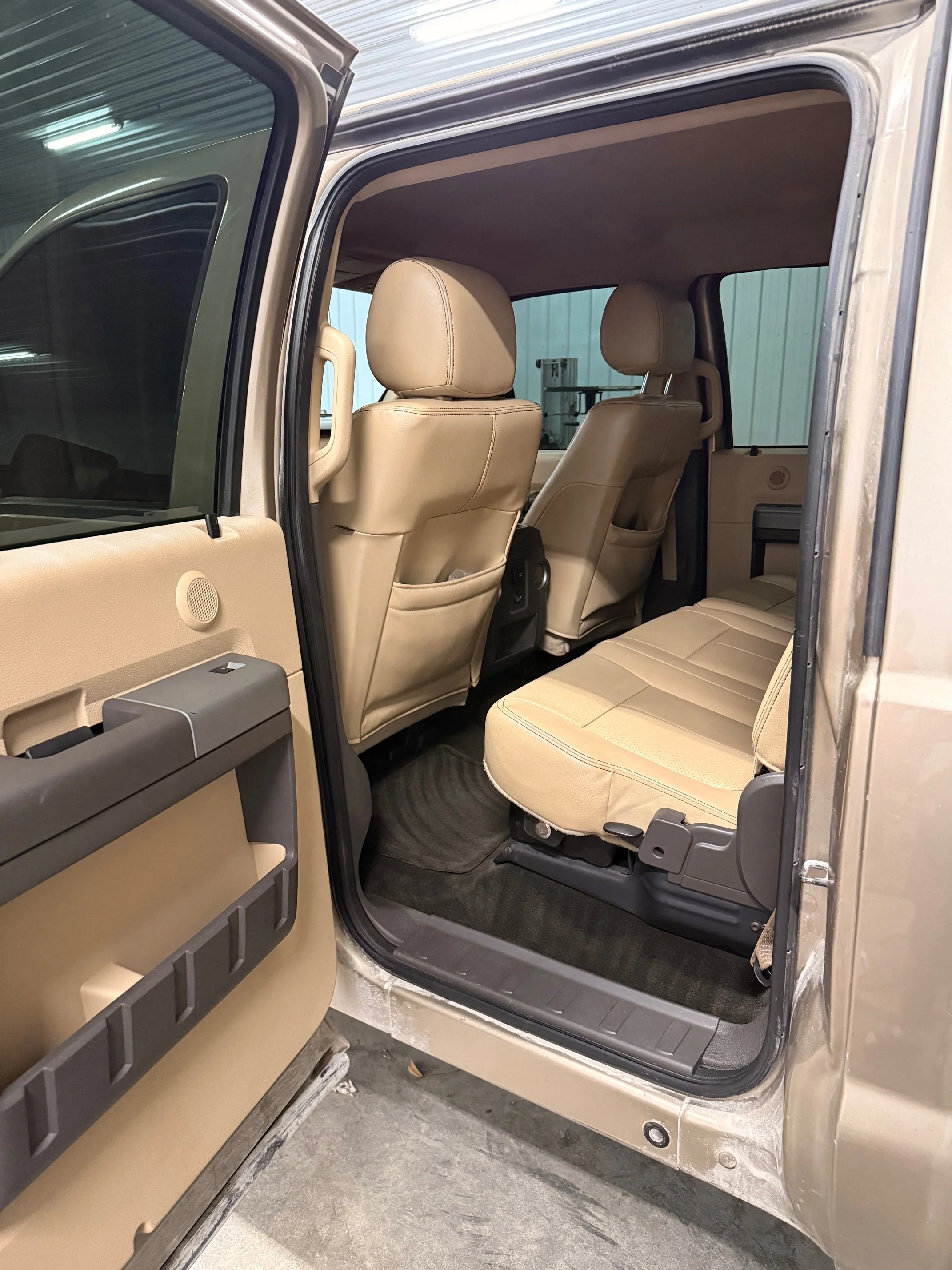 Inside view of the rear passenger area of a beige SUV, with beige seats, black floor mats, and beige door panels.