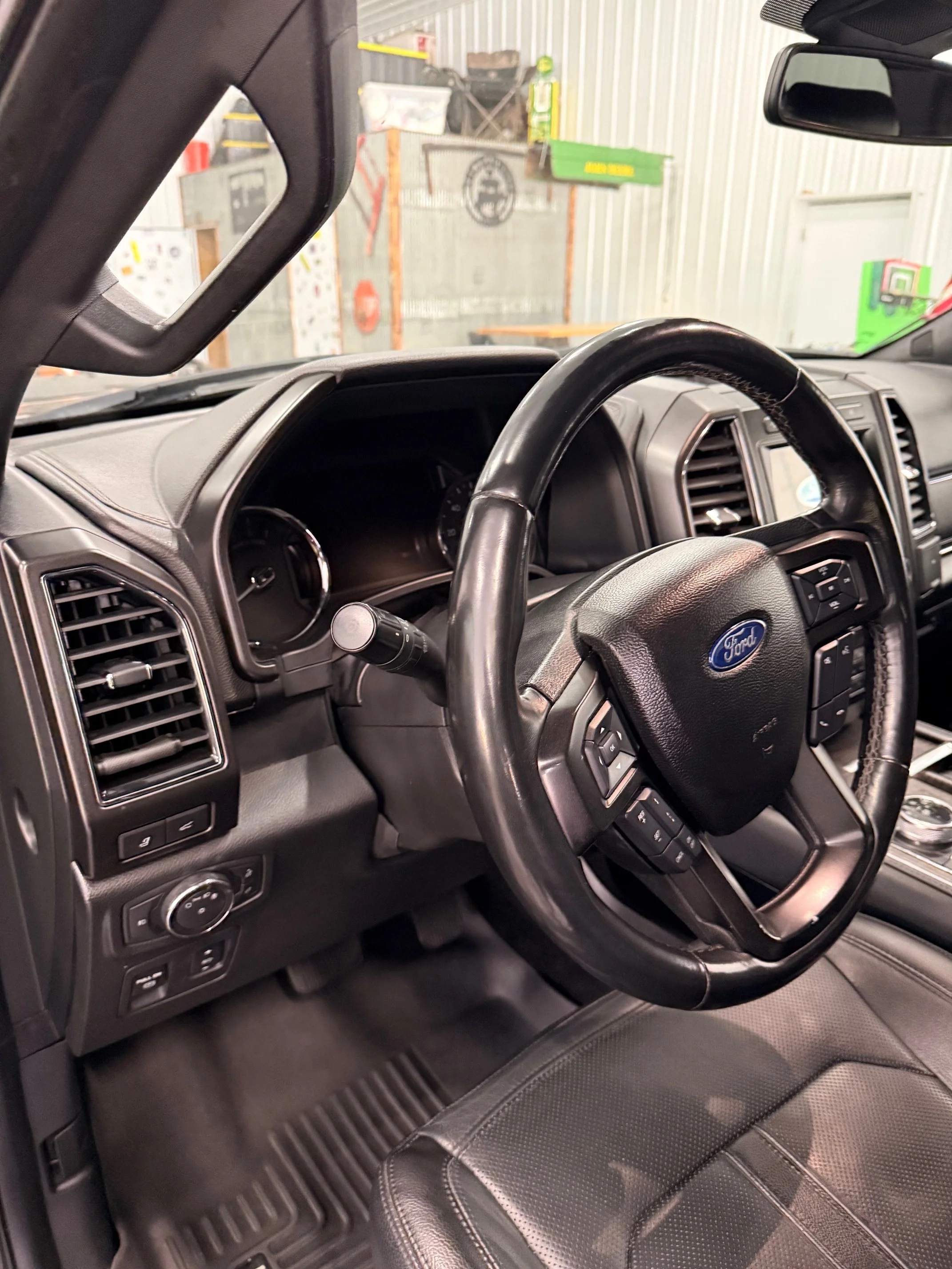 Interior of a Ford vehicle showing steering wheel, dashboard, air vents, and part of the driver's seat in a warehouse or garage setting.