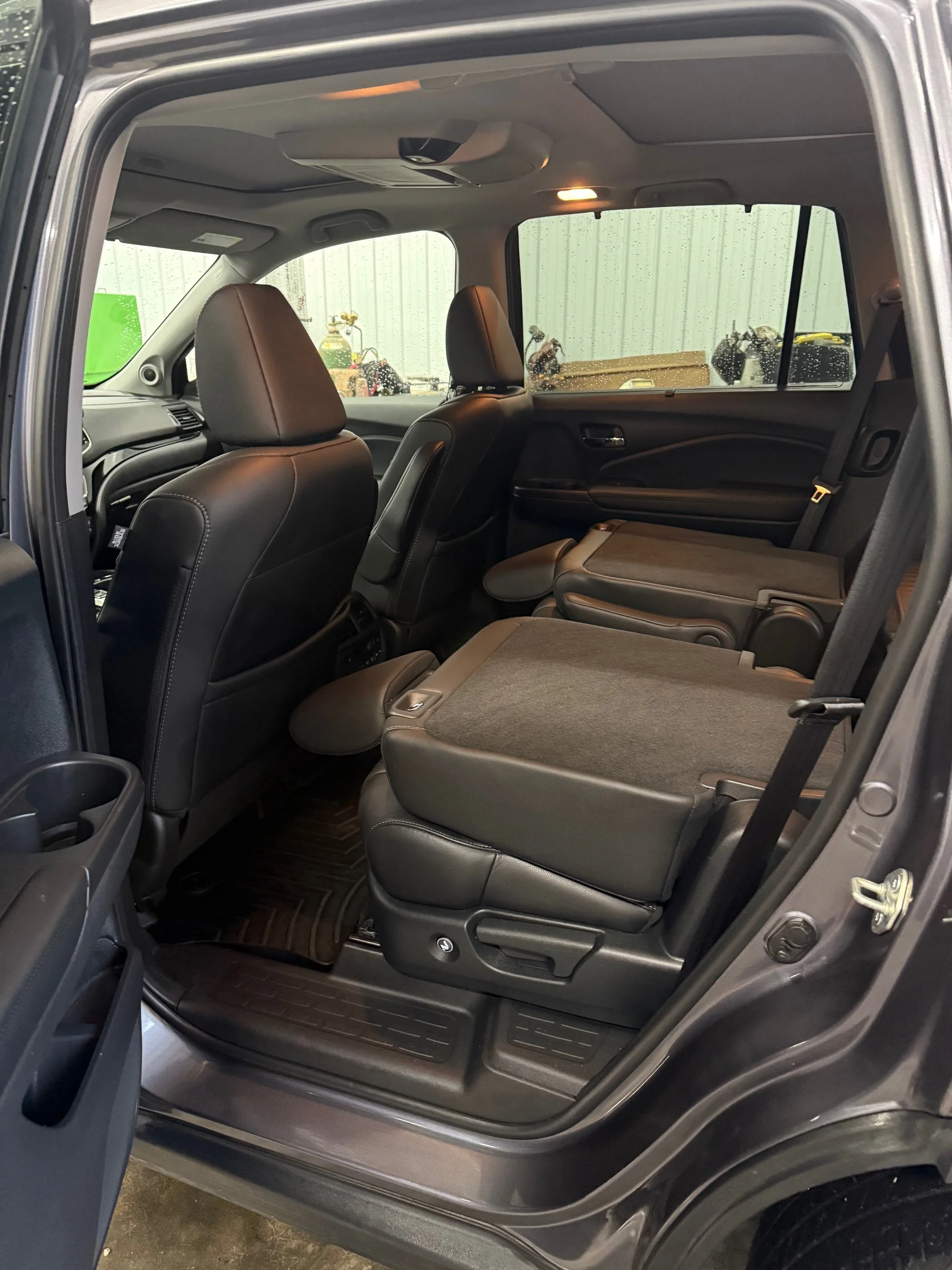 The interior of a black SUV with the second row seats folded down for cargo space, featuring black leather seats and floor mats.