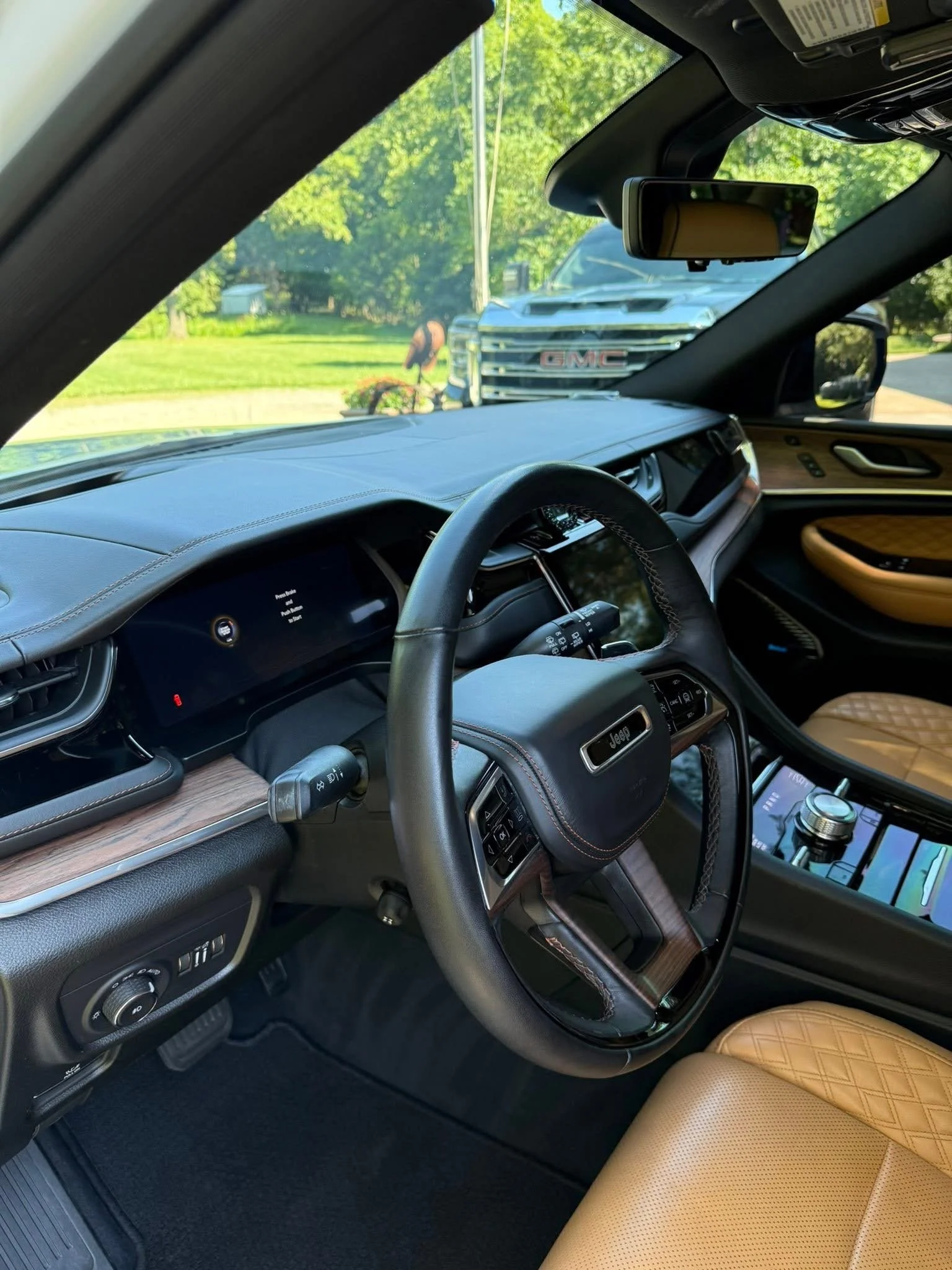 Interior of a modern vehicle with a digital dashboard, steering wheel, tan quilted leather seats, and a view of a GMC truck parked outside through the windshield.