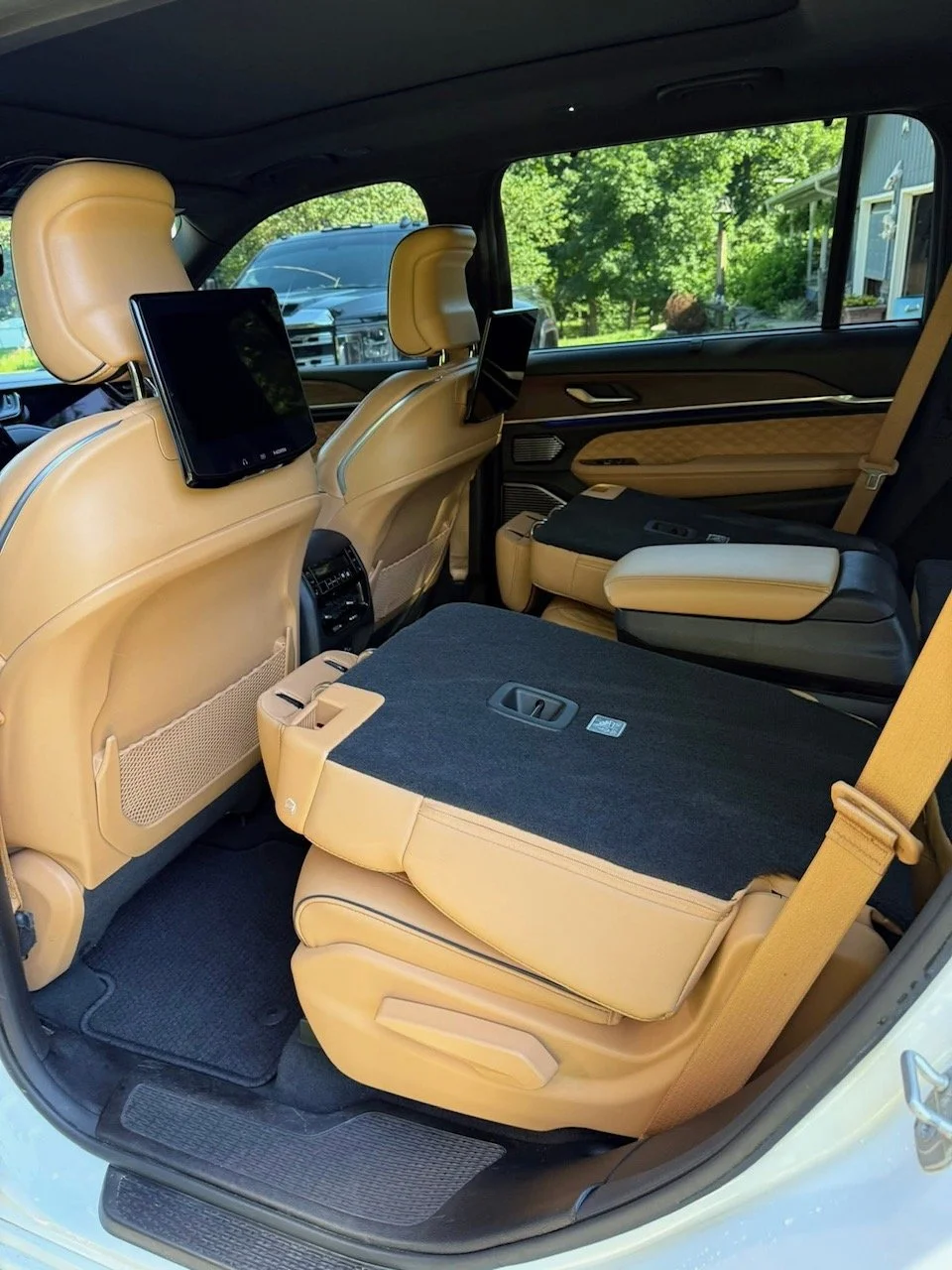 Interior of a luxury vehicle with beige leather seats, foldable rear seats, and built-in screens on the front seat headrests.