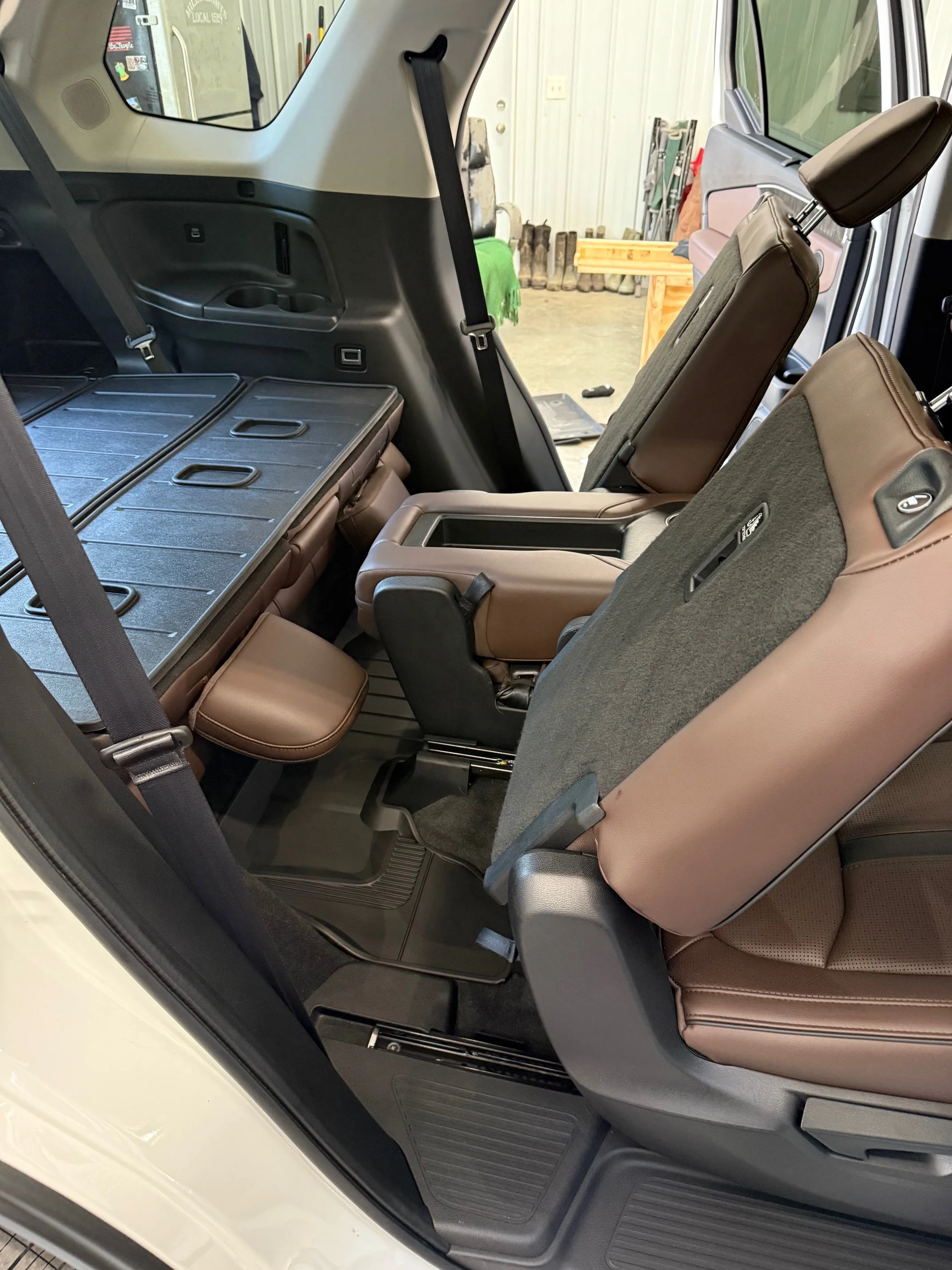 The interior of a vehicle, showing the back seats and cargo area with brown leather seats and headrests, located inside a garage.