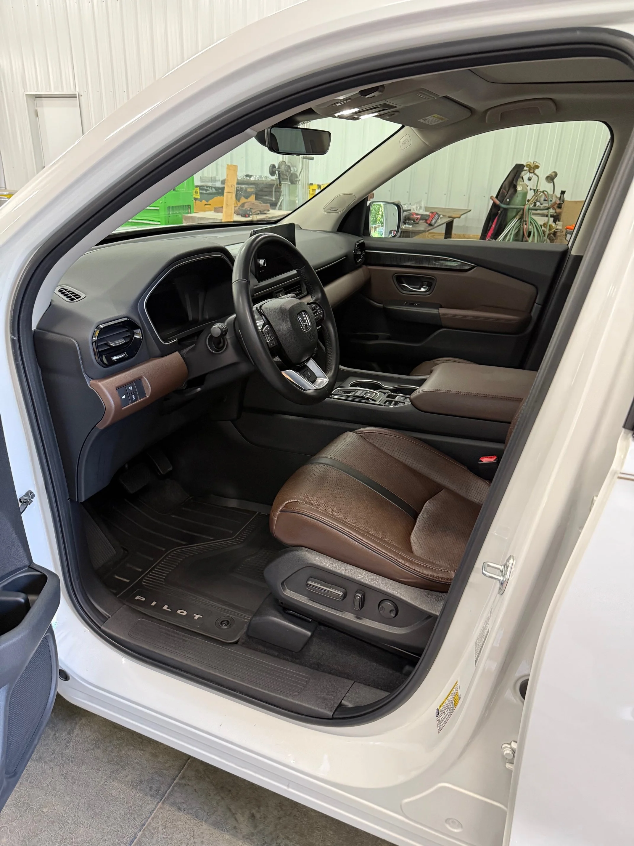 Interior view of a Honda Pilot SUV, showing the driver's seat, steering wheel, dashboard, and center console in a garage or workshop setting.