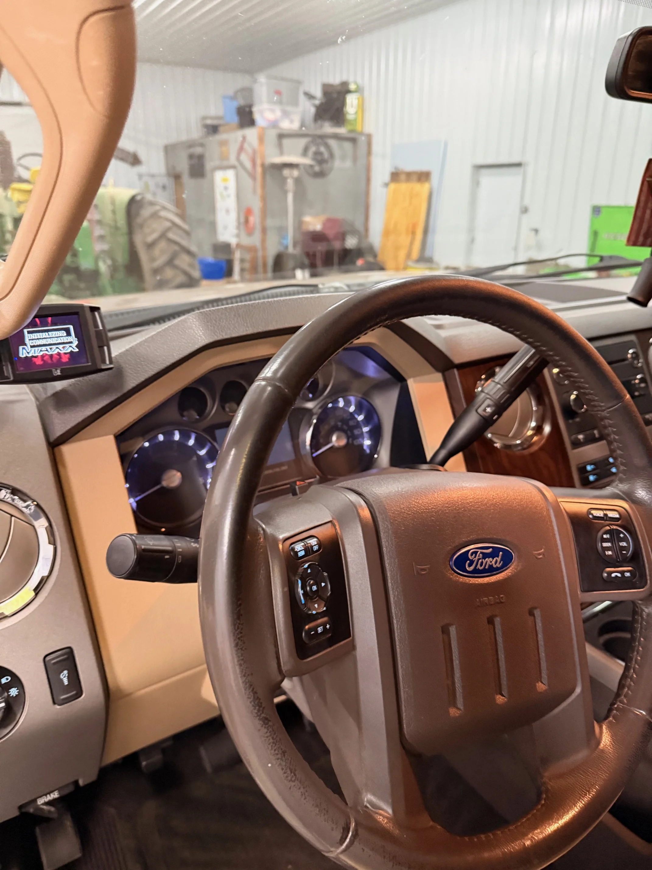 Interior view of a Ford vehicle dashboard, steering wheel, and instrument panel with a garage visible through the windshield.