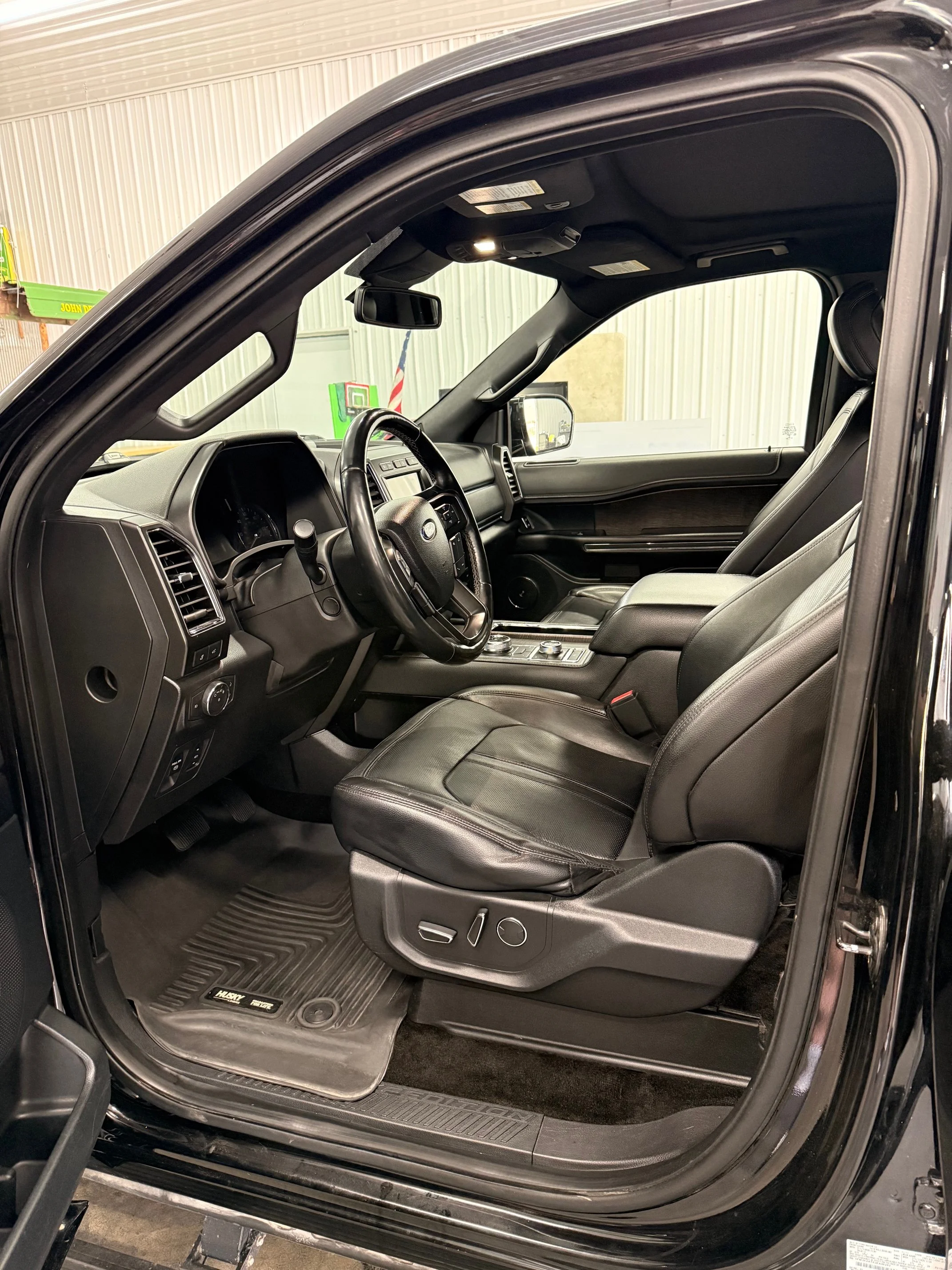 Interior of a black truck showing the driver and passenger seats, steering wheel, dashboard, center console, and professional rubber floor mats.