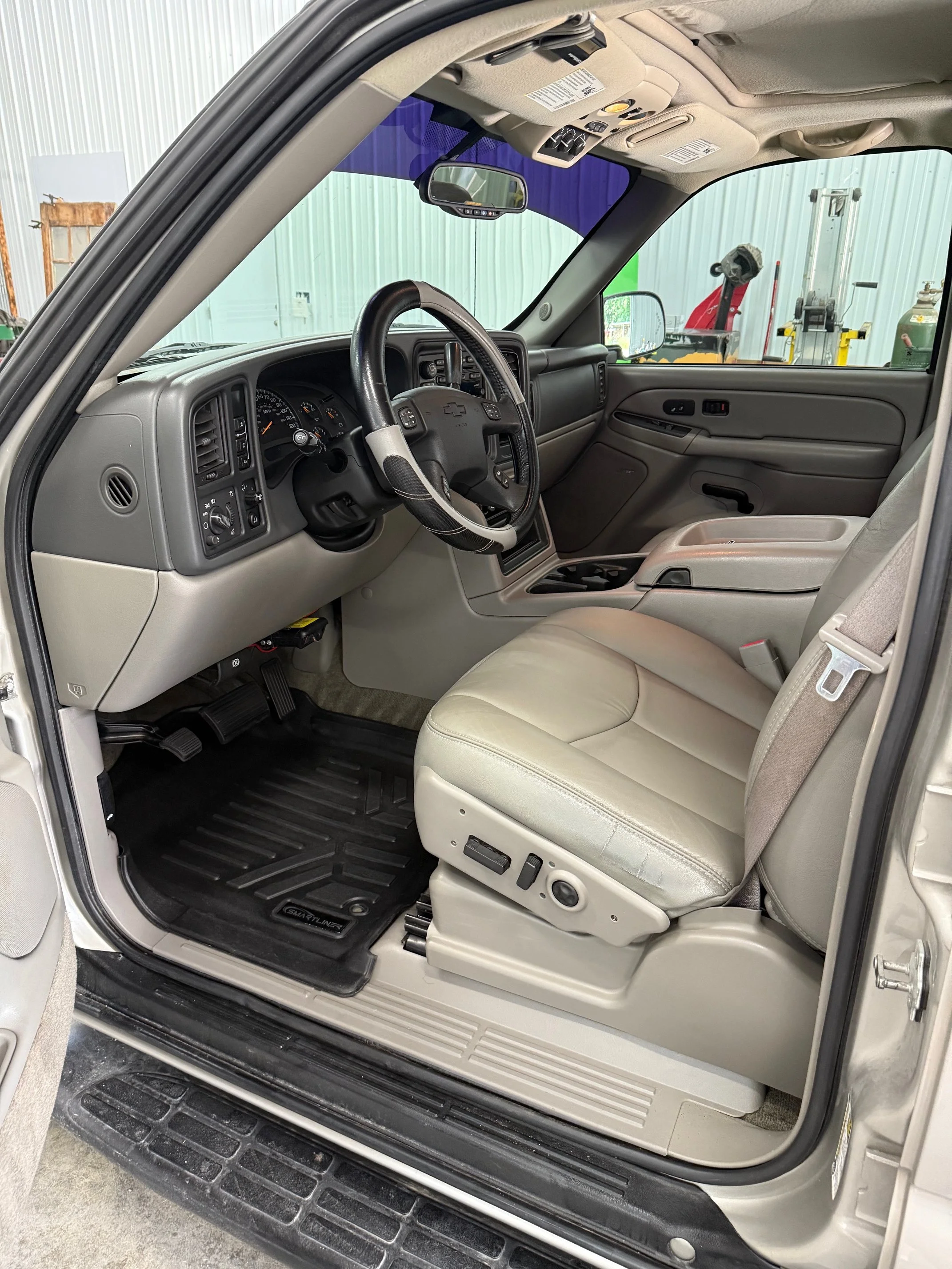 Front interior of a Chevrolet pickup truck showing the driver's seat, steering wheel, dashboard, and center console, with a view of the parking lot and building outside through the window.