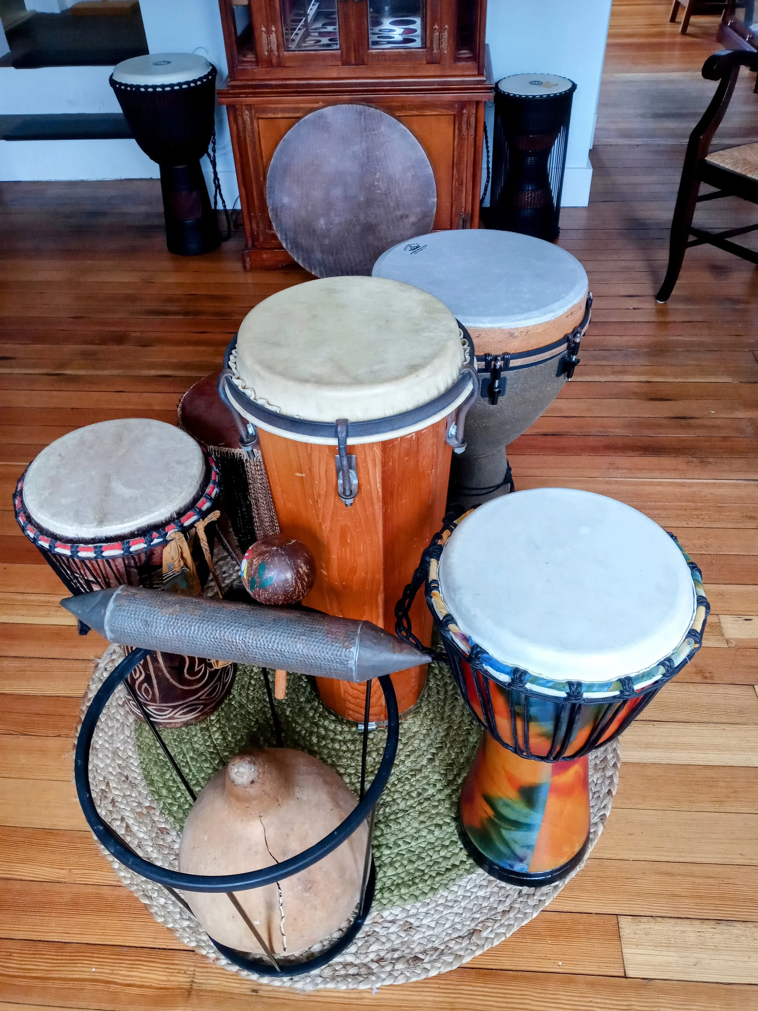 Collection of African drums of various sizes and styles arranged in a circular woven basket on a wooden floor in a room.