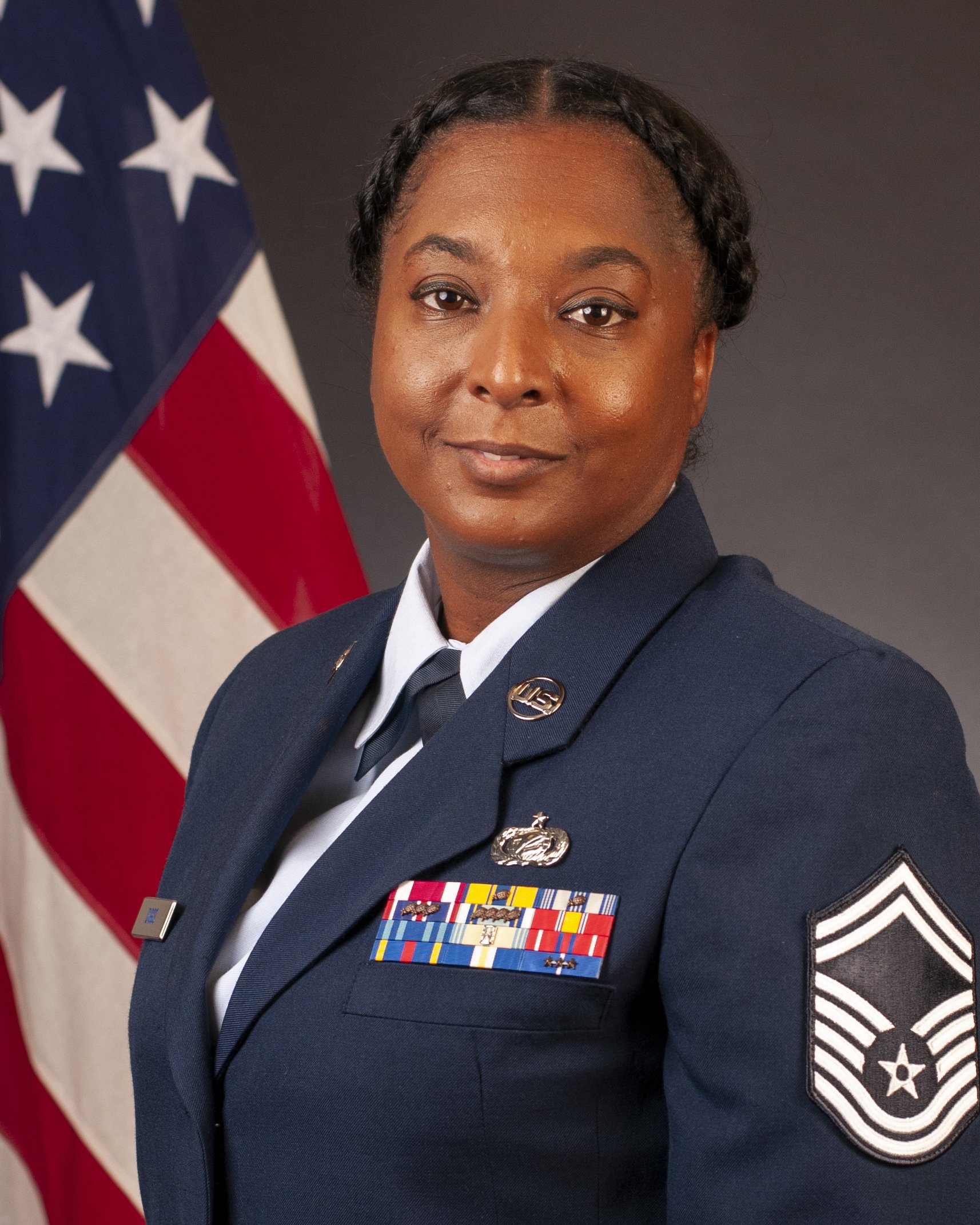 A female military officer posing in uniform with medals and patches, standing in front of an American flag.