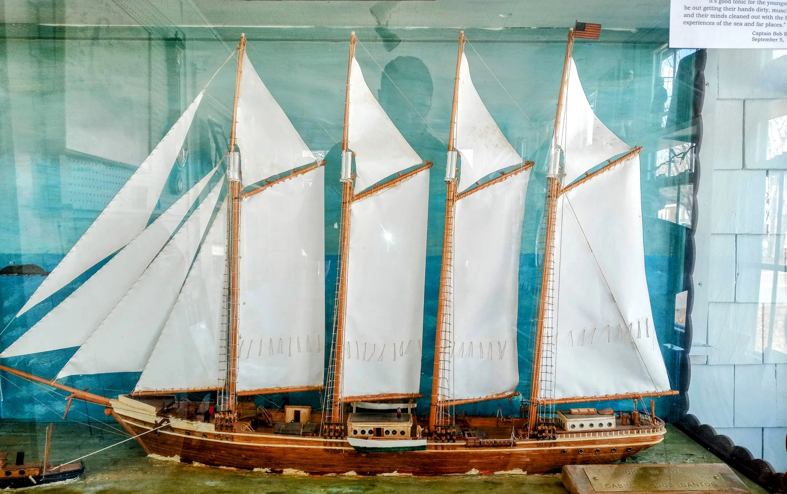 Model of a large wooden sailing ship with white sails inside a glass display case.