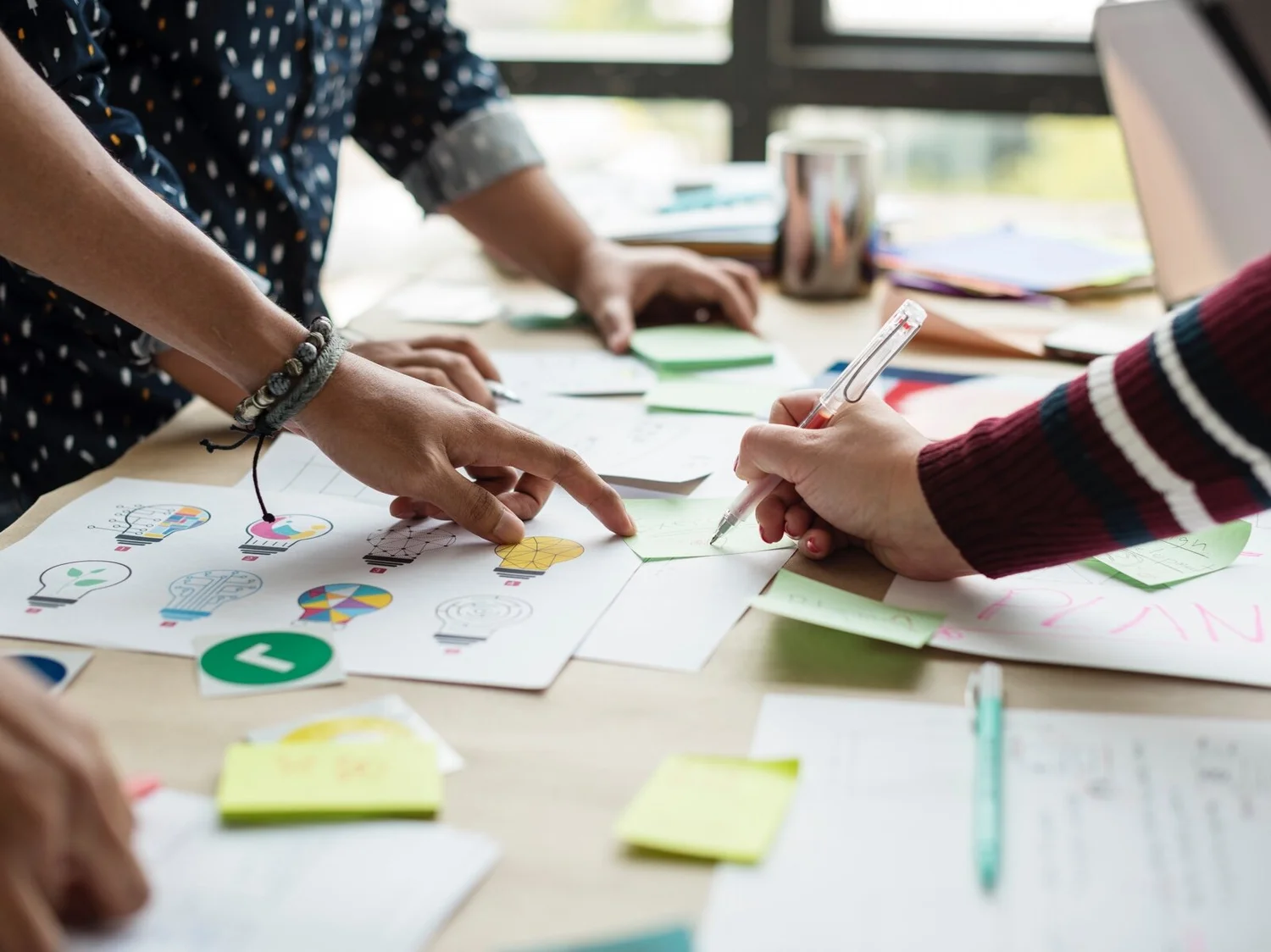 People working on a creative project with drawings, sticky notes, and writing materials on a table.