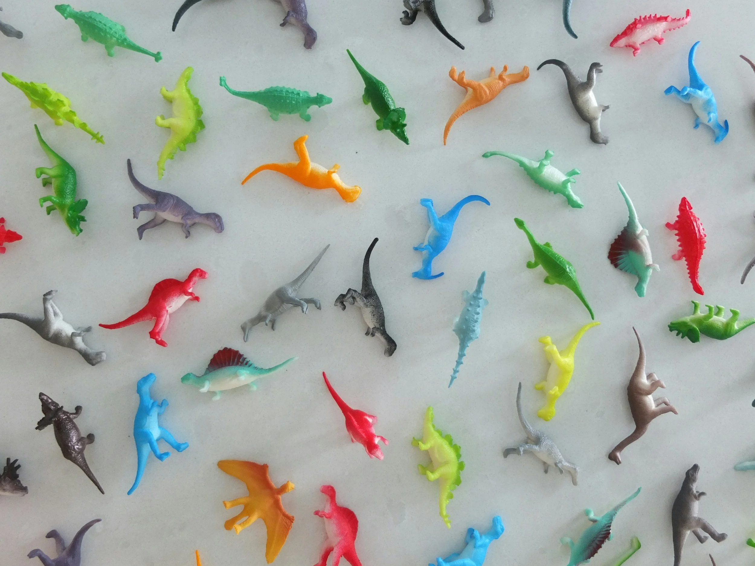 Colorful plastic toy dinosaurs scattered on a white surface.