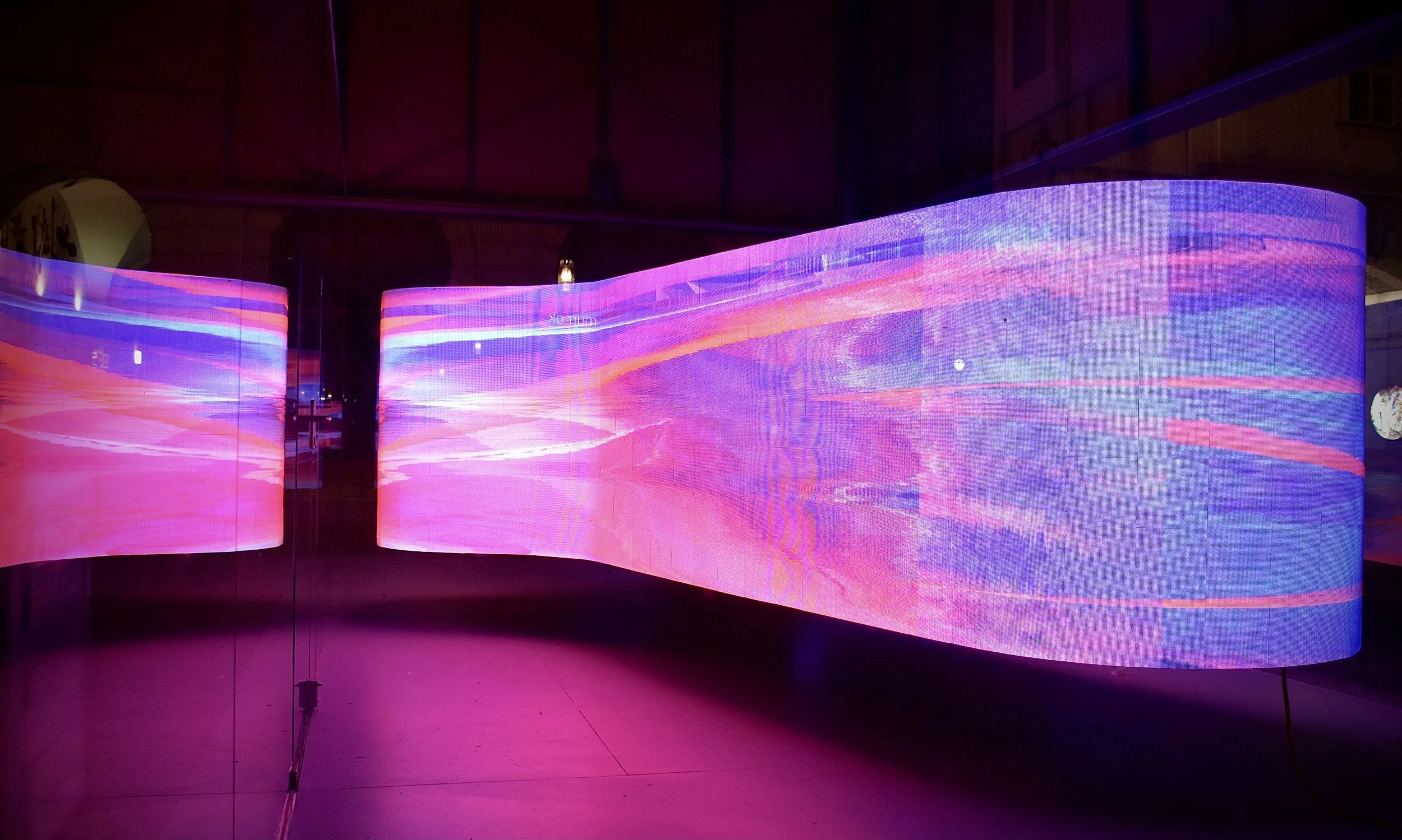 Curved LED screens displaying vibrant pink, purple, and orange abstract light patterns in a dark room.