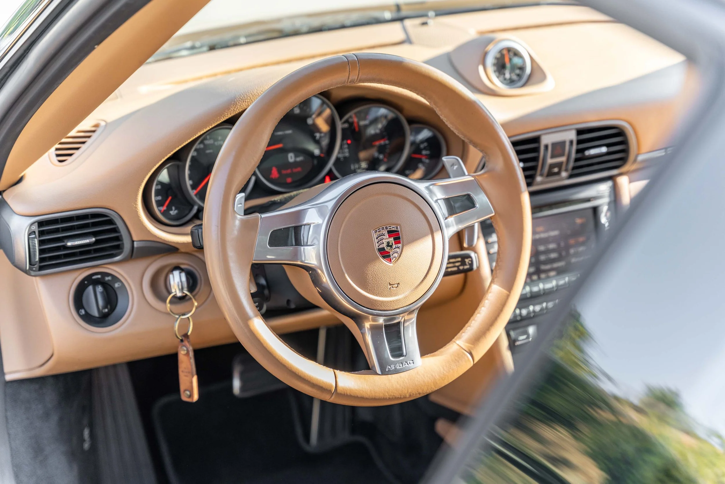 Interior of a Porsche sports car showcasing a beige dashboard, a beige steering wheel with a Porsche emblem, and various gauges and controls.