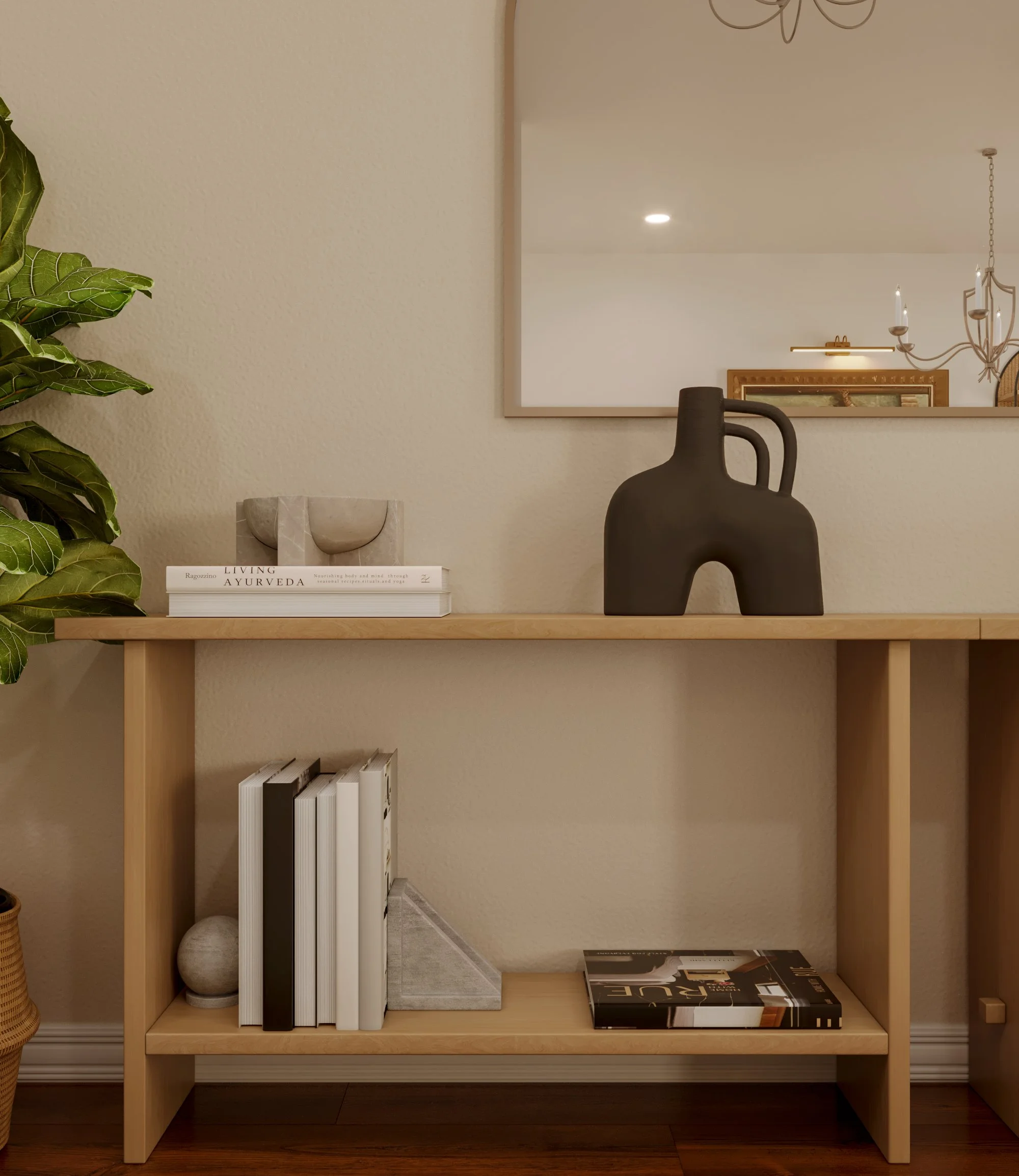 A wooden bookshelf with a potted plant on the left, a stack of books with neutral and dark covers, a decorative concrete ball, and a large black ceramic vase with a handle on top. A mirror reflects a chandelier and part of a framed painting or mirror