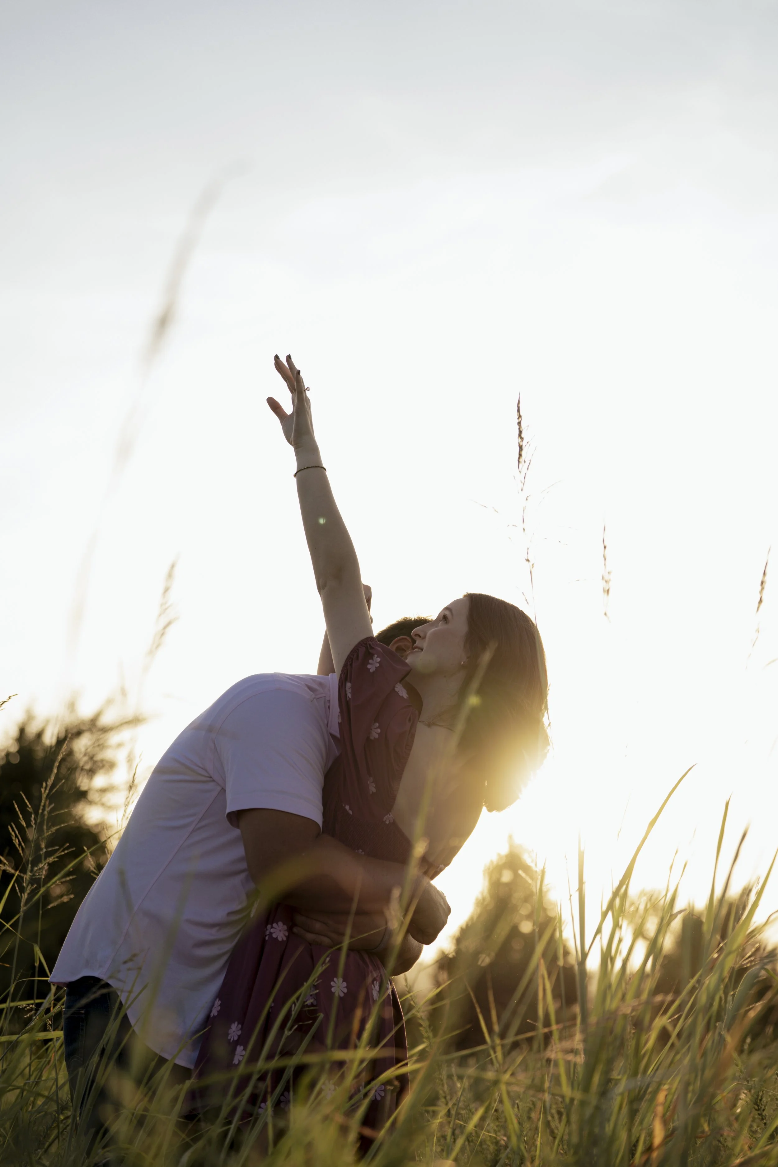 A couple kissing in a field during sunset, with one person lifting their arm in the air.