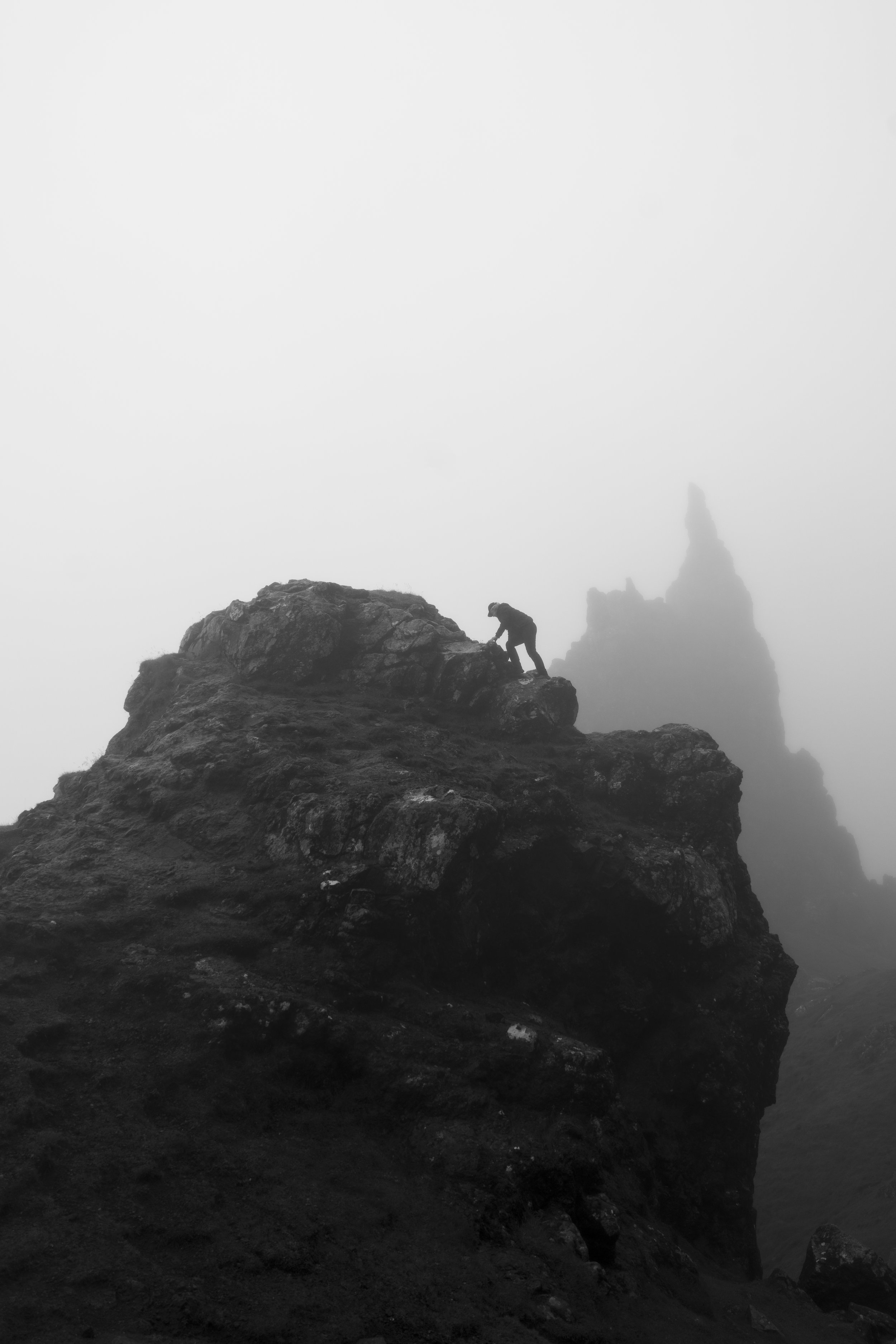A person climbing rocky terrain in foggy weather, with a tall rock formation in the background.