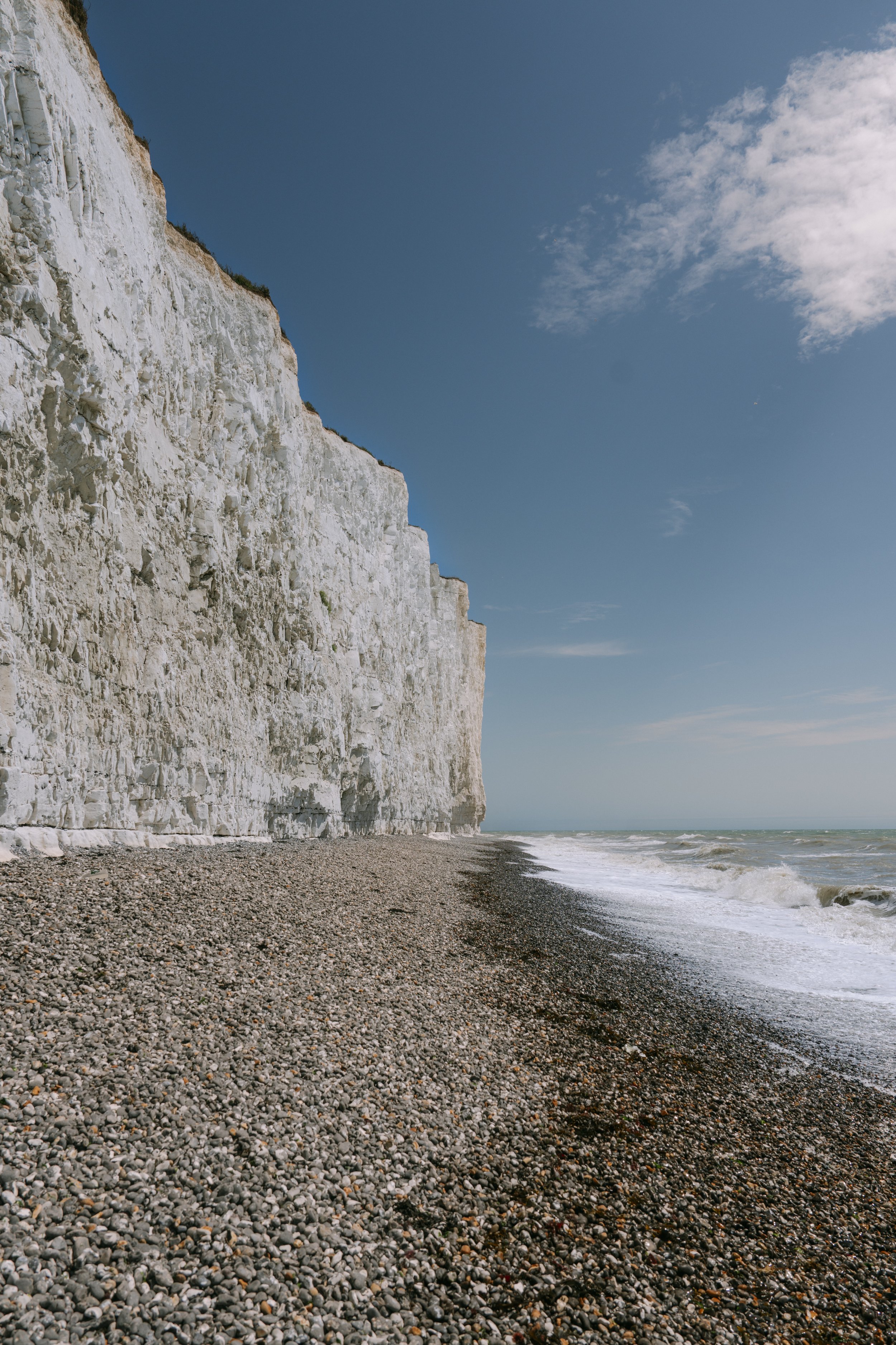 White chalk cliffs along a pebble beach with the ocean and a partly cloudy sky.