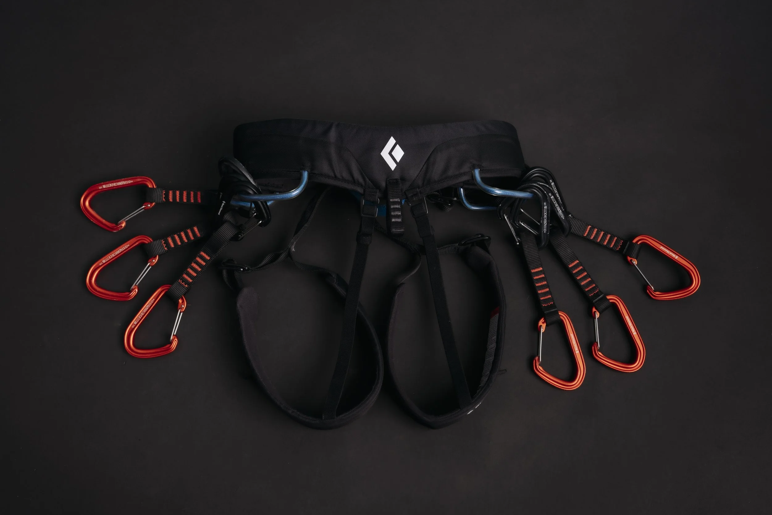 A climbing harness with several red carabiners attached against a black background.
