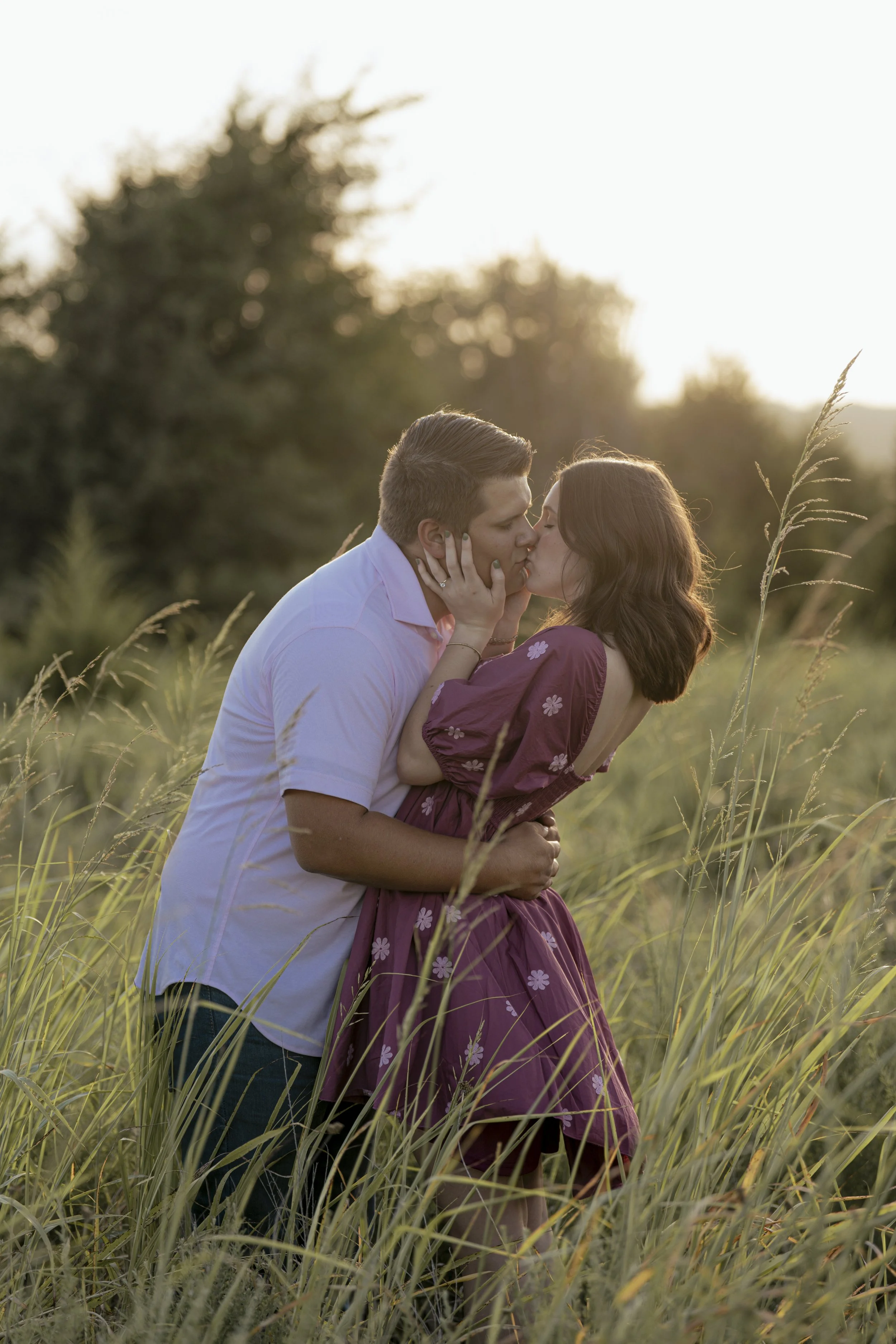 A young couple sharing a kiss in a field of tall grass during sunset.