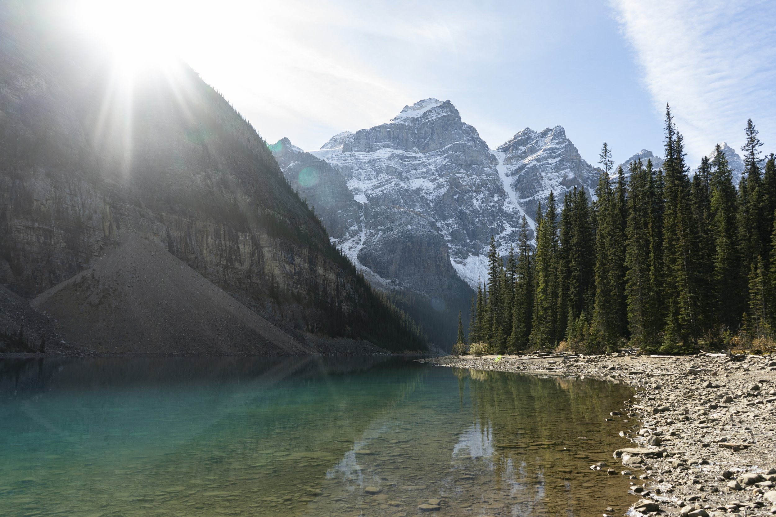 Scenic mountain landscape with a lake, snow-capped peaks, and a forest of evergreen trees under a partly cloudy sky
