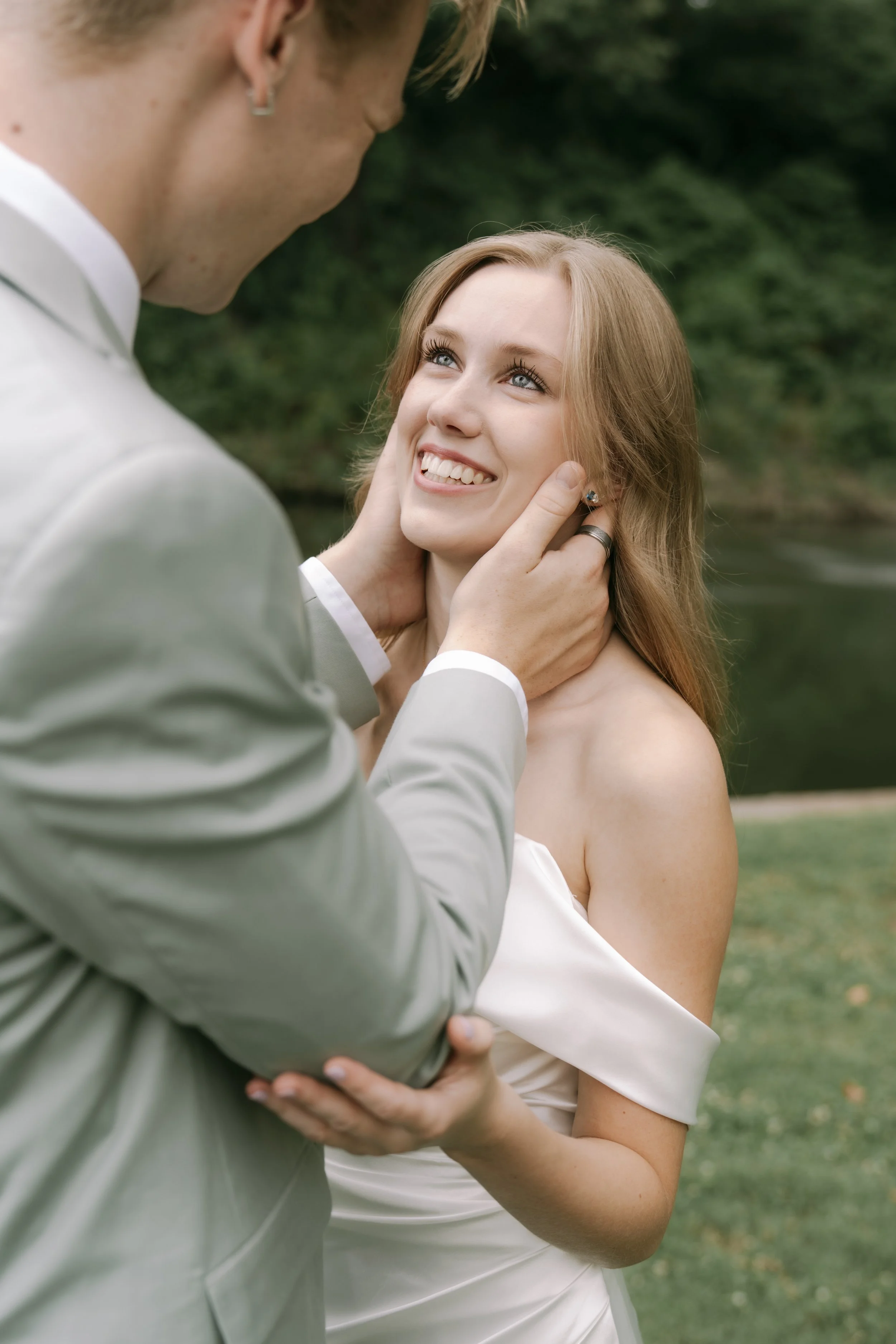 A couple on their wedding day, with the groom gently holding the bride's face and the bride smiling happily.