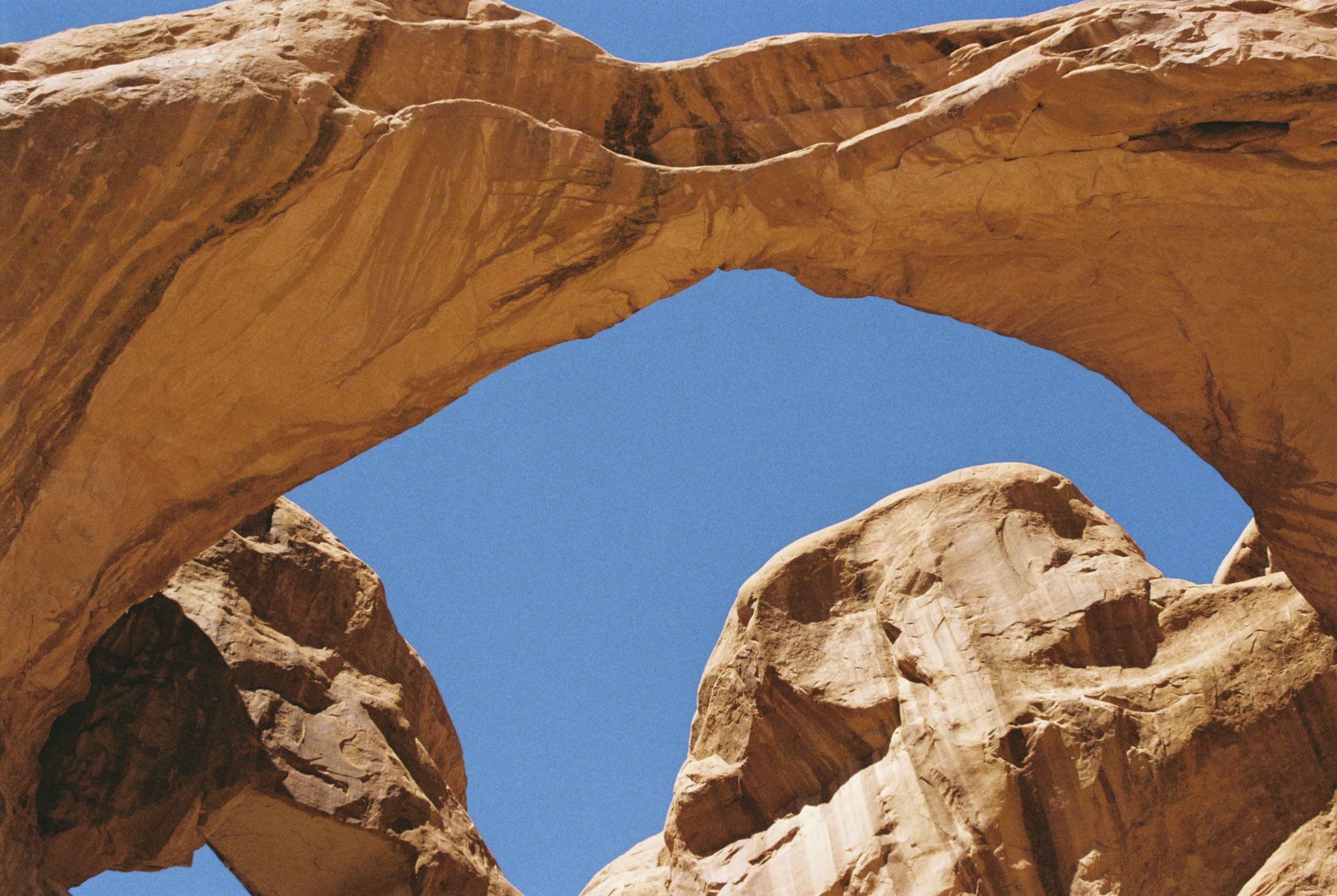 Looking up through a natural rock arch in a desert landscape with clear blue sky.
