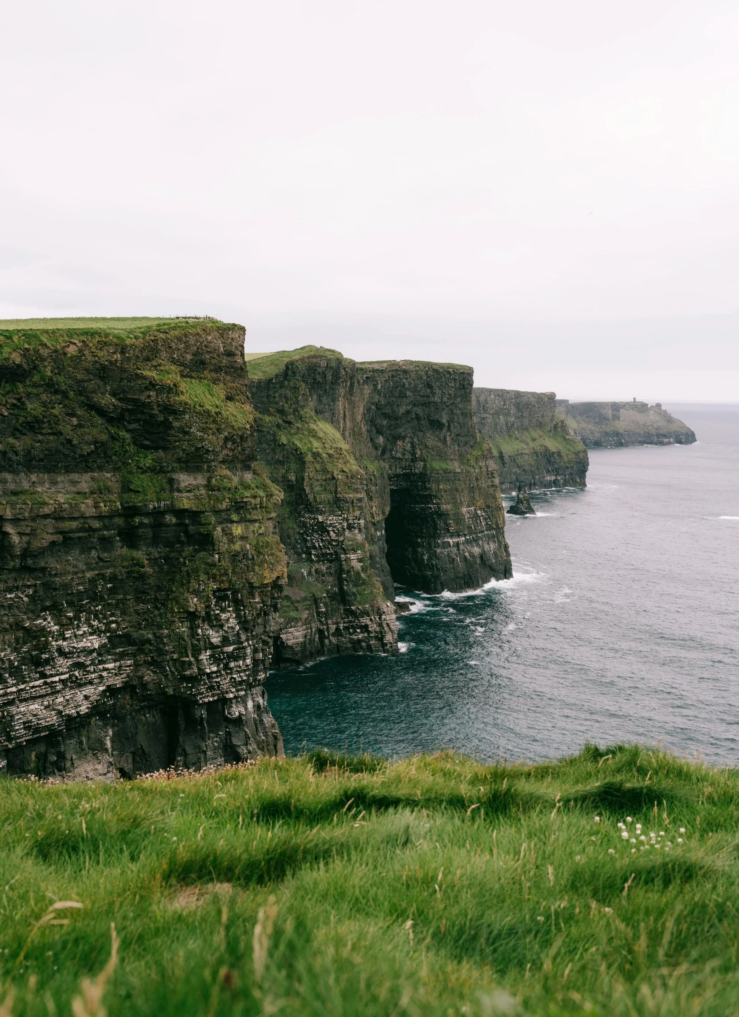 Cliffs along the coastline with green grass in the foreground and an overcast sky.