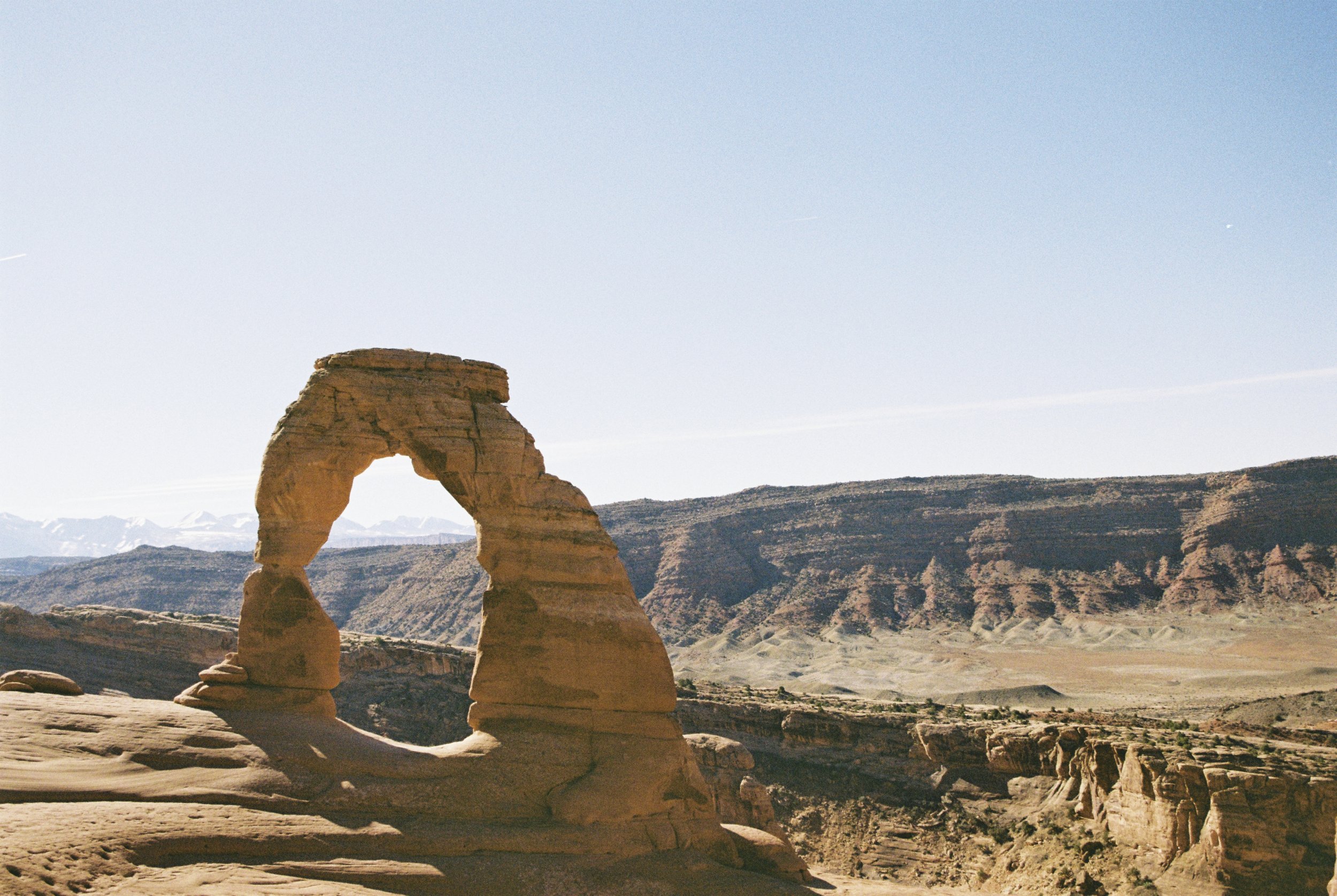 Delicate Arch, a natural sandstone arch, standing in a desert landscape with mountains in the background under a clear sky.