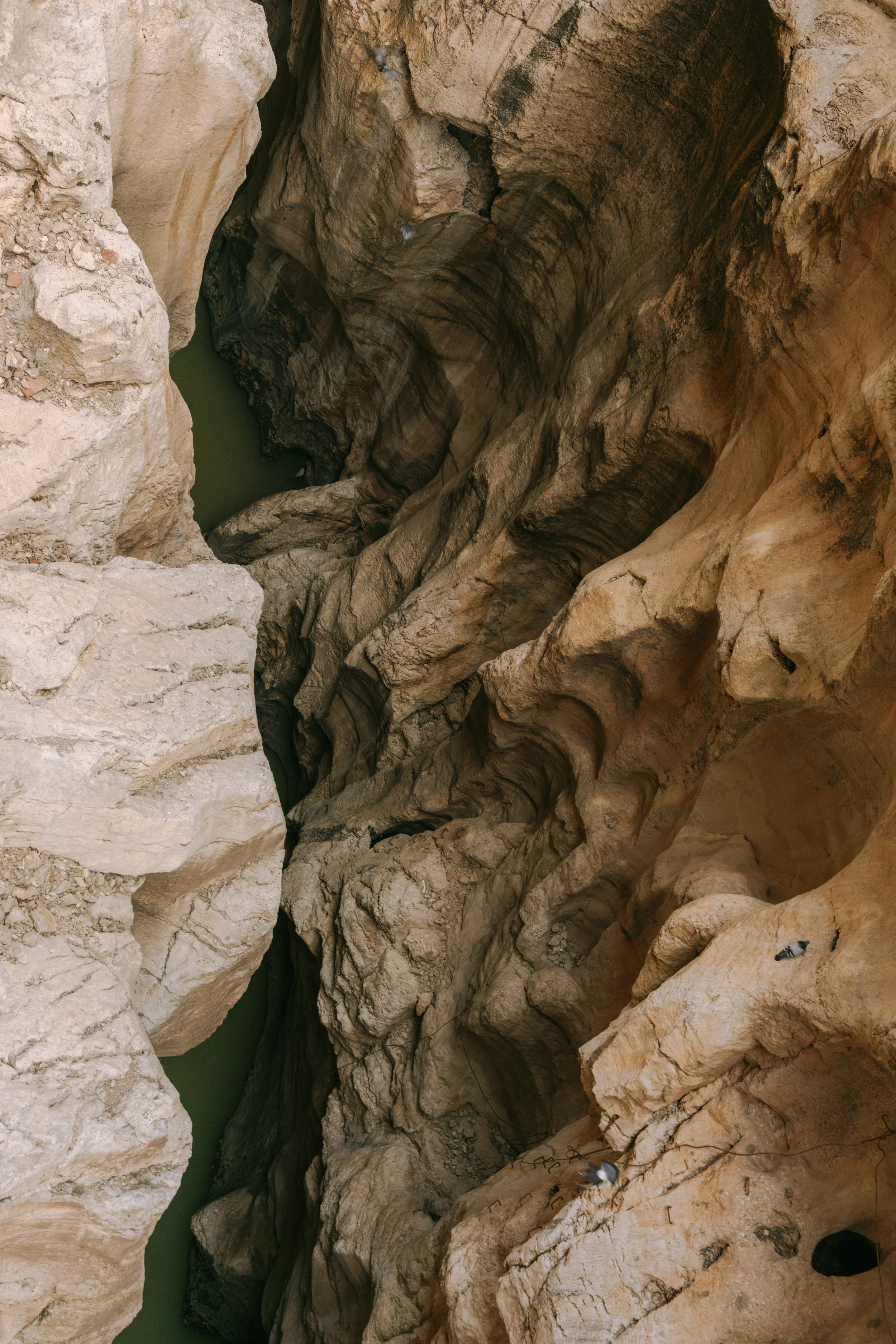 A high-angle view of a narrow canyon with steep rock walls and a green water channel at the bottom.