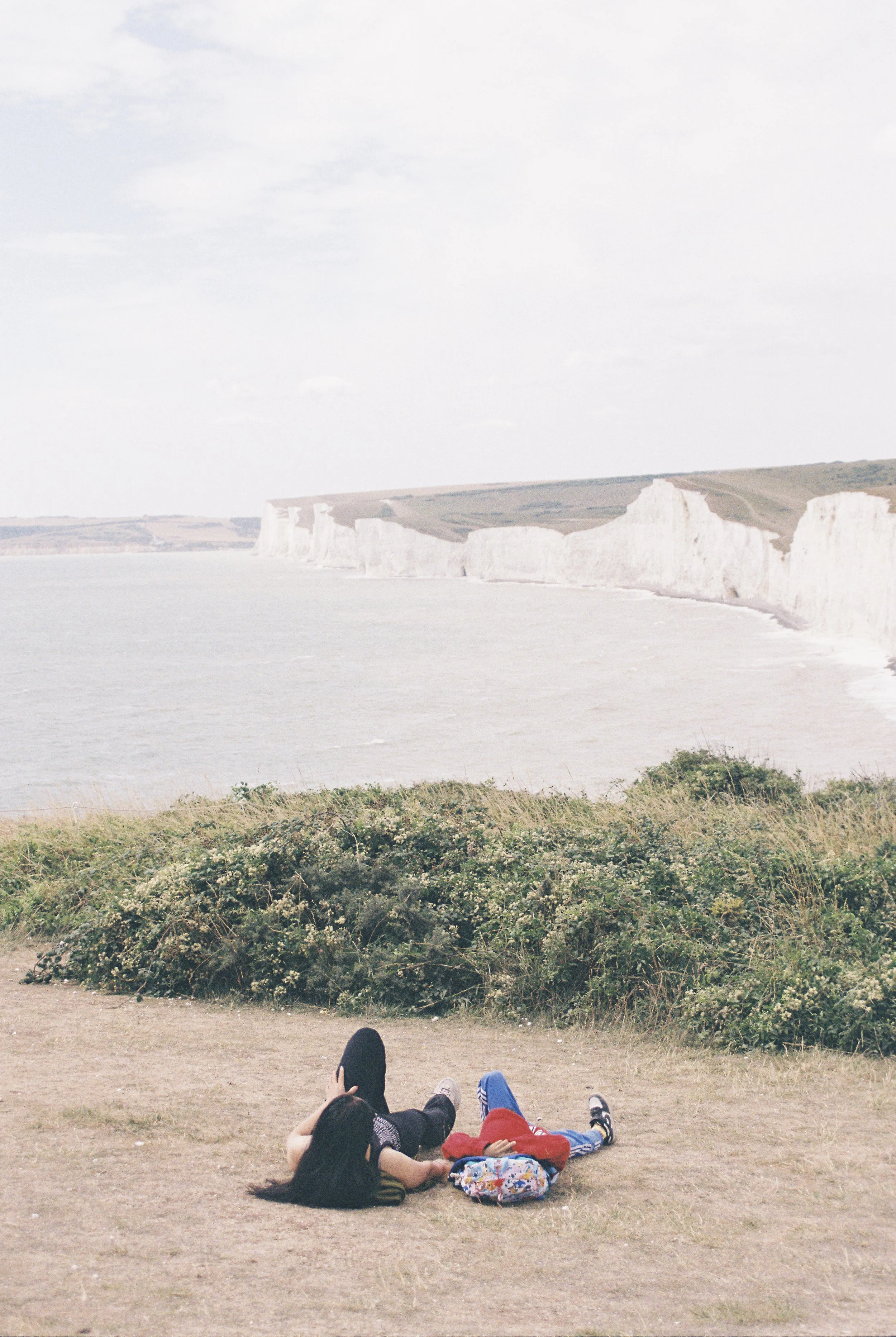 A young woman and a child lying on the grass by the coast, overlooking the white cliffs of Dover.
