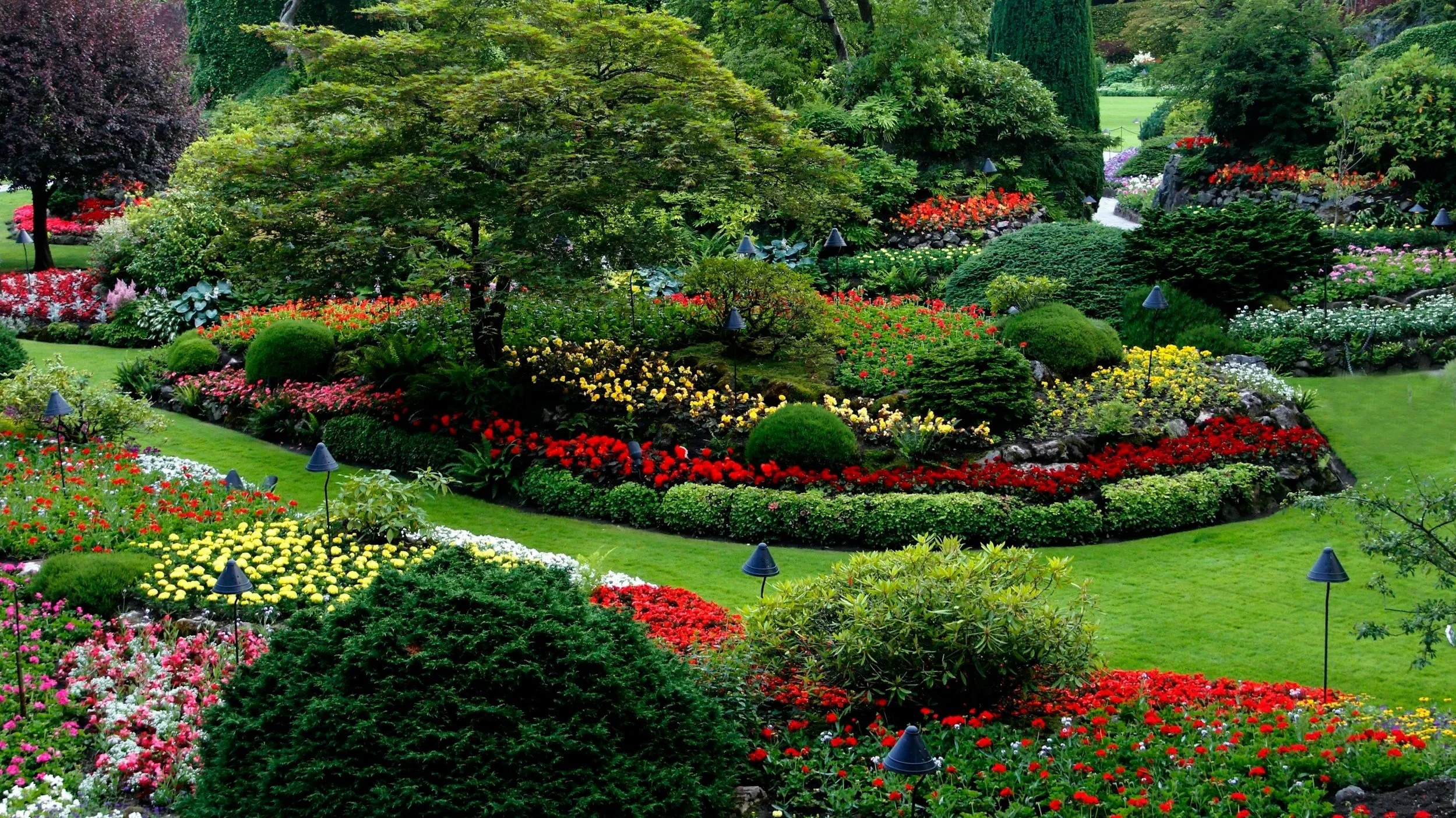 Colorful garden with various flowers and lush green trees, shrubs, and well-maintained grassy areas.