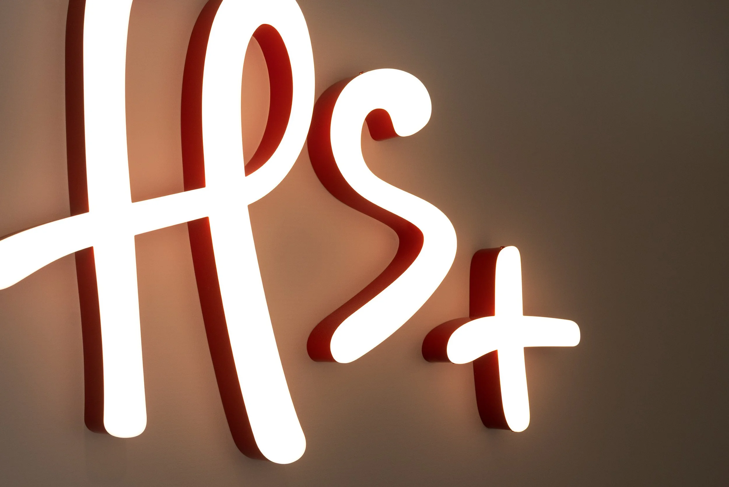 Close-up of a modern, glowing neon sign with white and red light bulbs shaped into letters, mounted on a wall.