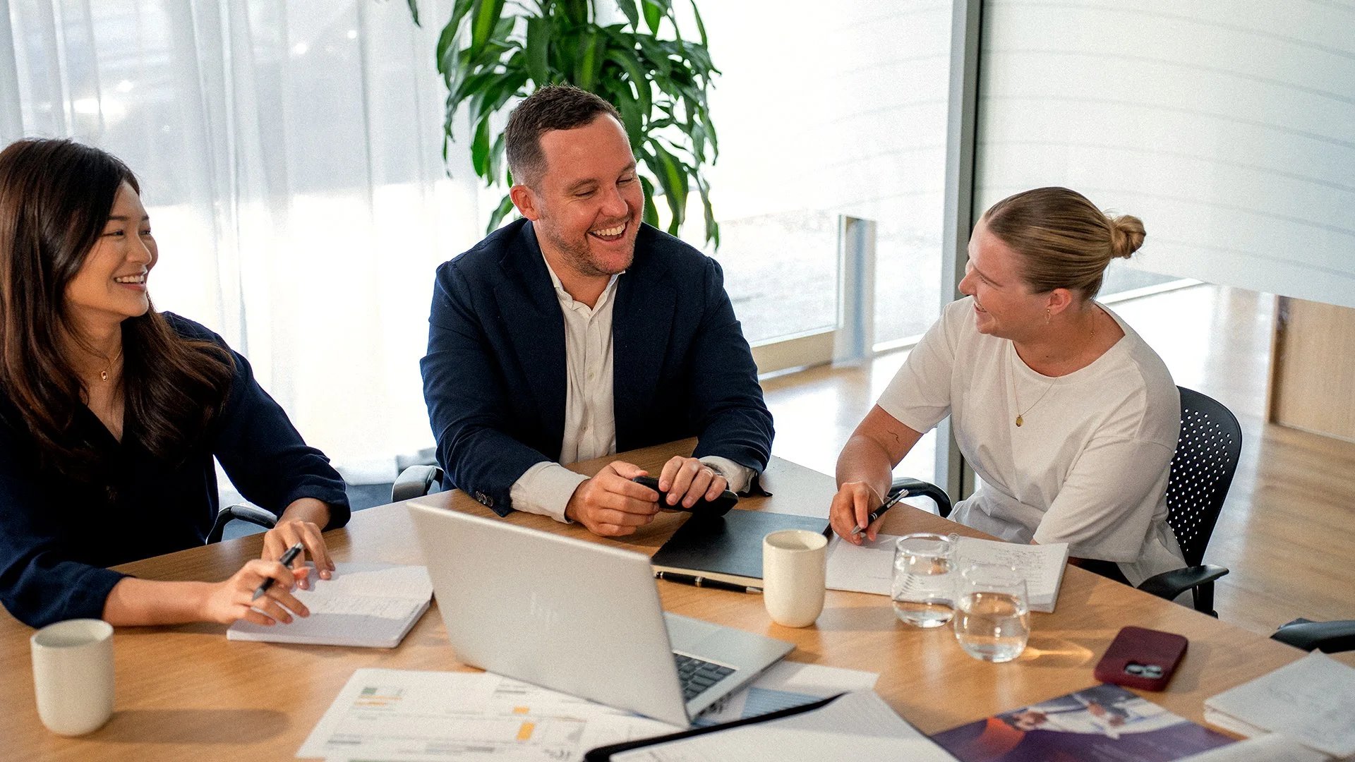 Four people sitting around a conference table, engaged in conversation and smiling, in a modern office setting.
