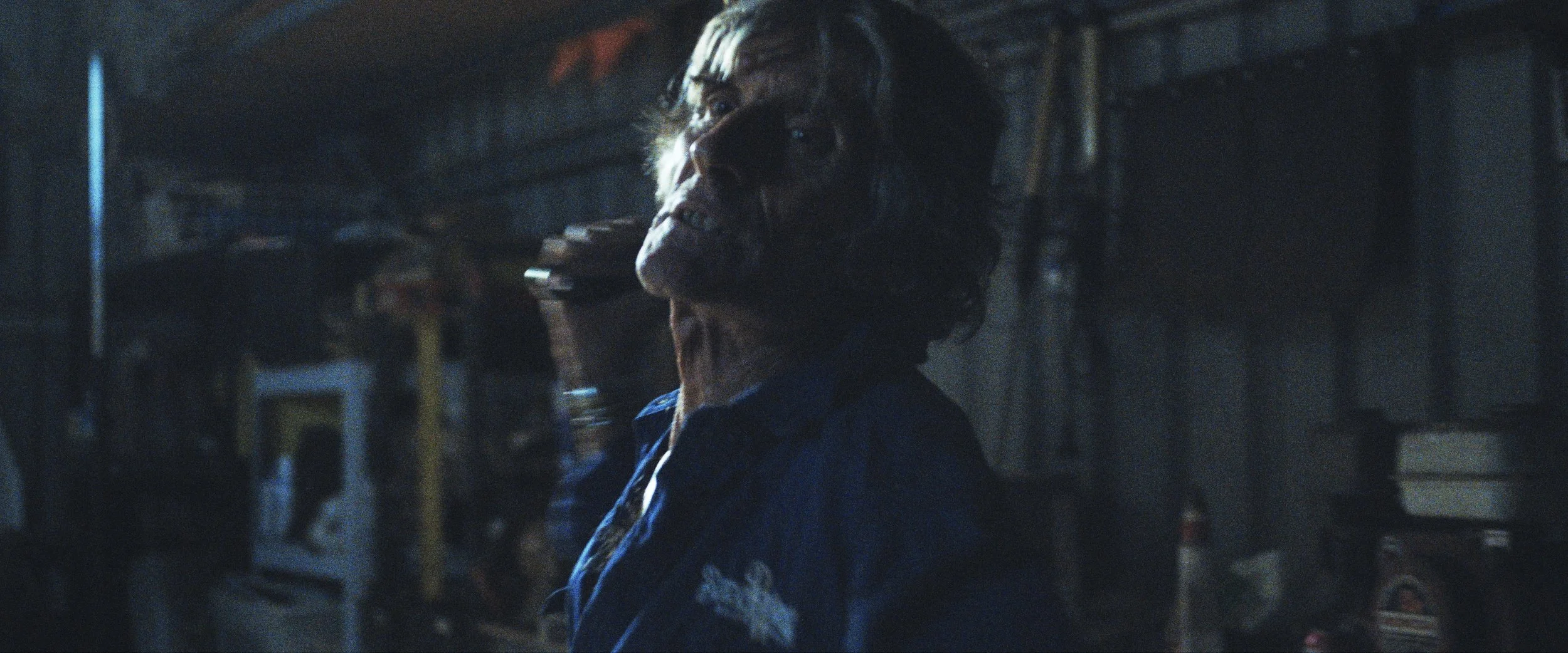 A violent man  appears to be threatening someone with a wrench inside a dimly lit garage or storage area.