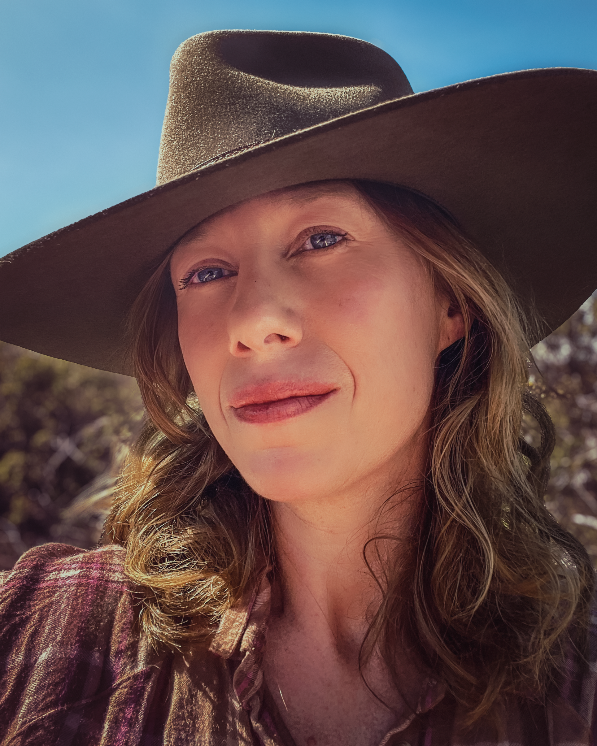 Rebecca Parker, Co-Managing Director at Honey Ant Productions and a writer/director/producer.  Close-up of a woman wearing a wide, brown hat outdoors with a blue sky background.