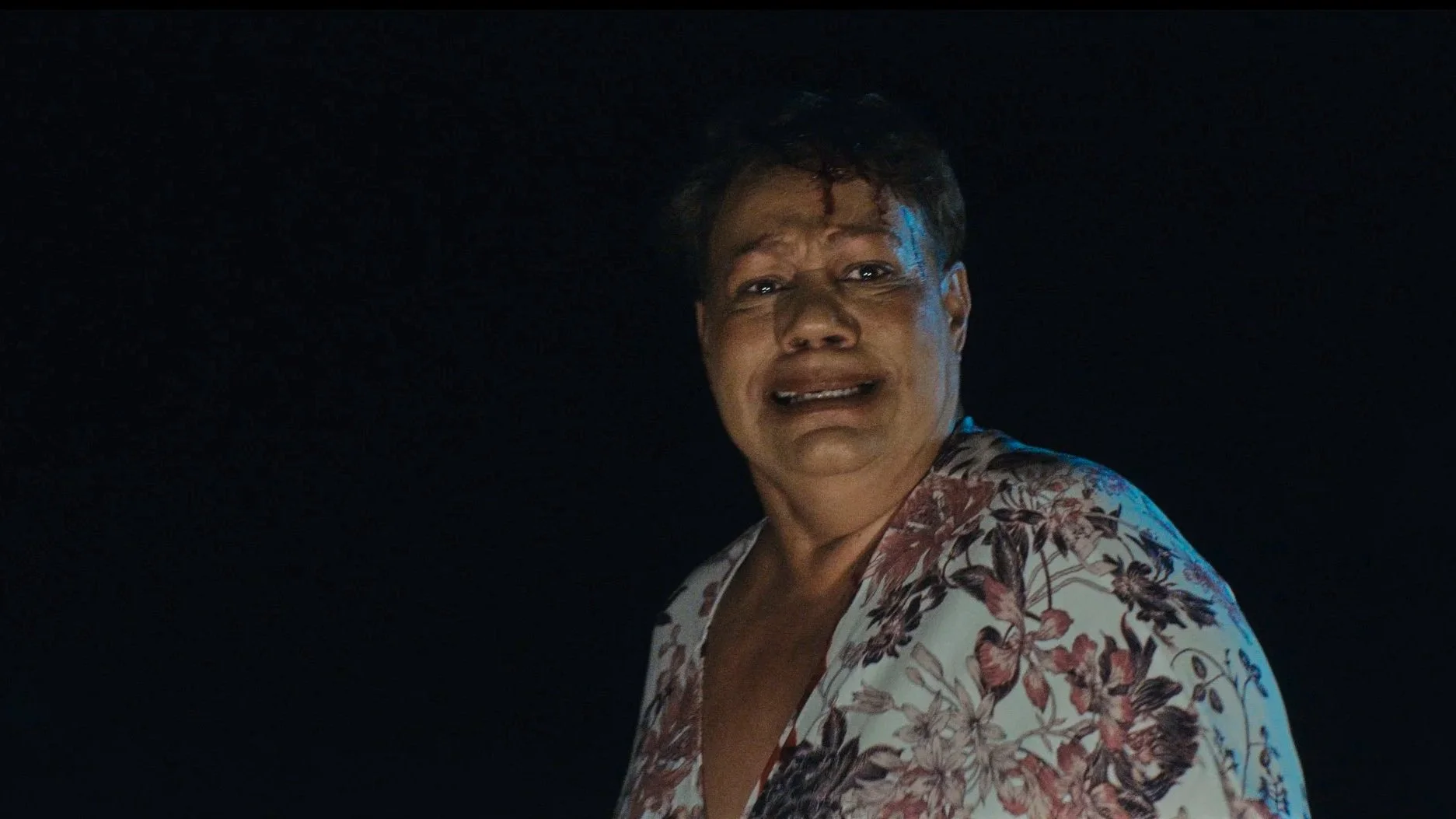 A woman with short hair, wearing a floral shirt, has a distressed expression on her face, with tears and a worried look.