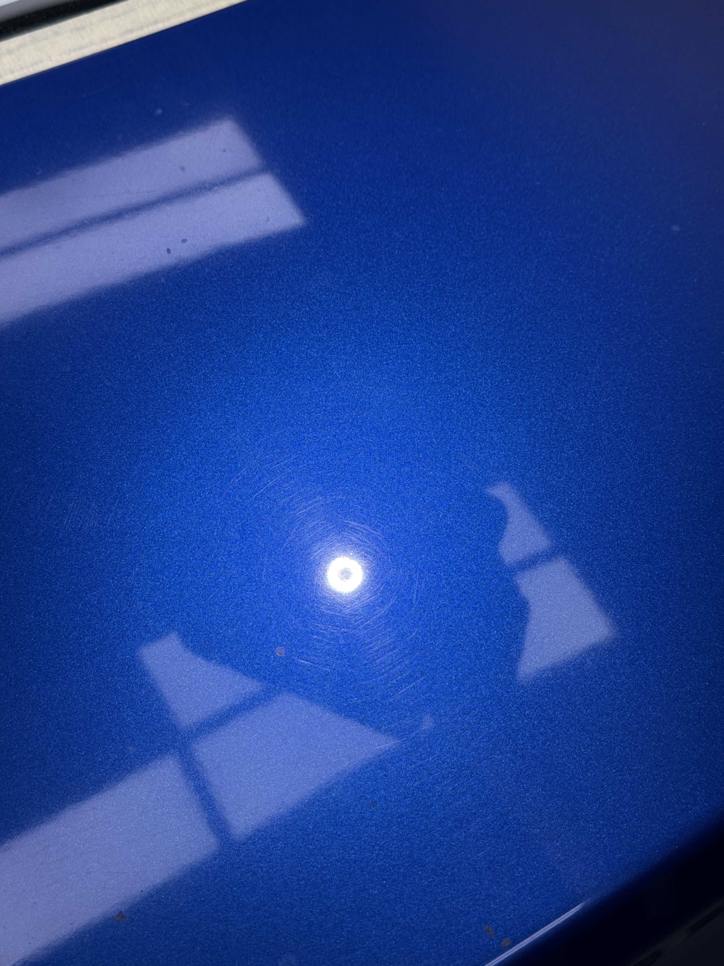 Blue metallic paint before correction, with swirl marks visible around the reflected inspection light.