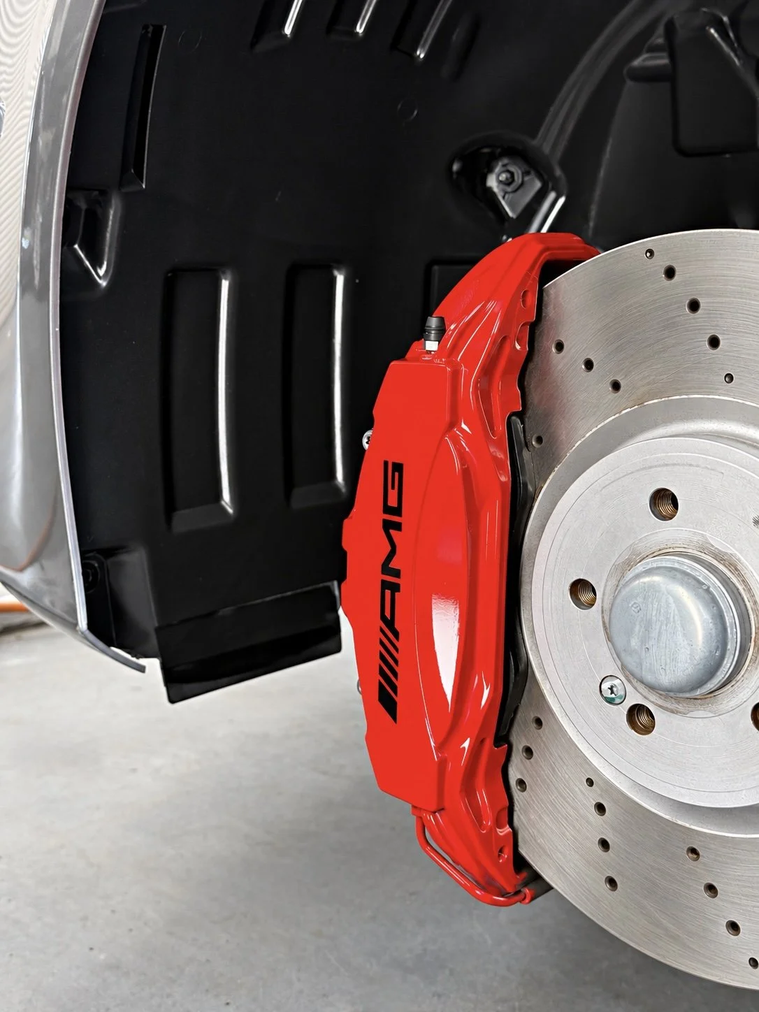 Red AMG brake caliper and clean black wheel arch liner after preparation, with the wheel removed.
