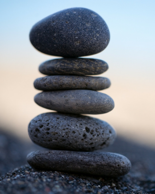 Stacked smooth black stones balanced on sandy ground with a blurred sky in the background.