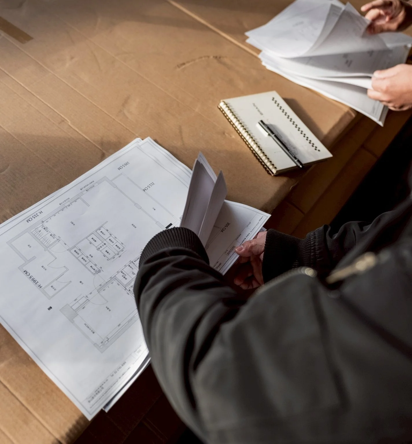 Person reviewing architectural blueprints on a table, with notebooks and documents nearby.