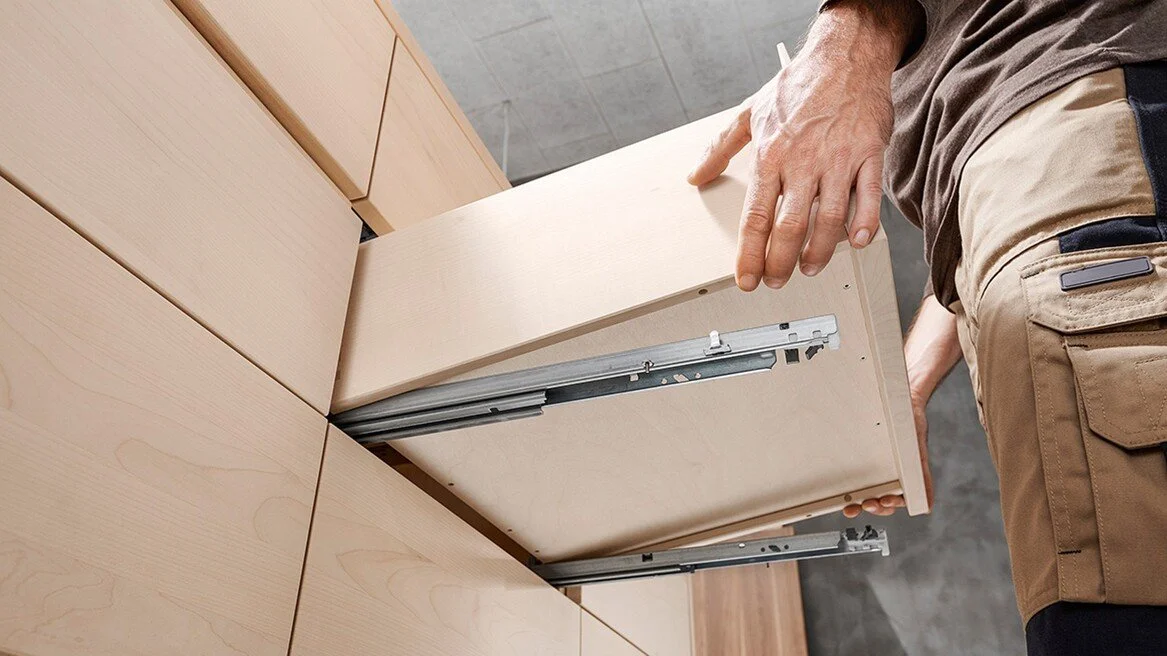 A person assembling a wooden cabinet using metal sliding tracks.
